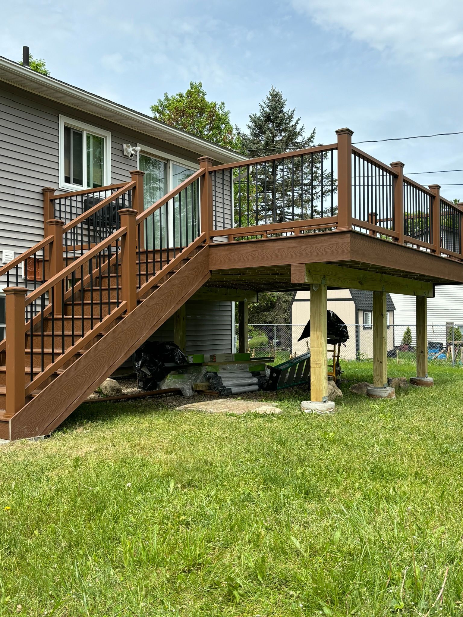 Brown composite deck with black railing and stairs attached to a gray house, set over a grassy lawn.