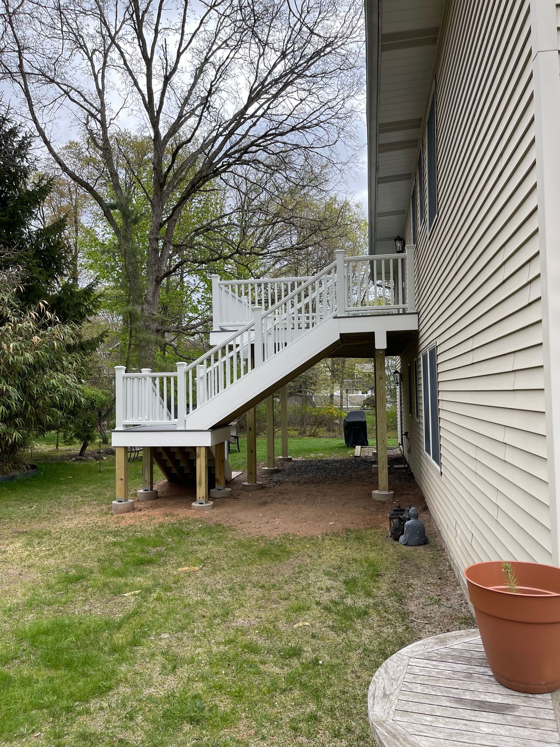 Exterior of a house with a white wooden deck and stairs, supported by wooden posts, next to a grassy lawn.