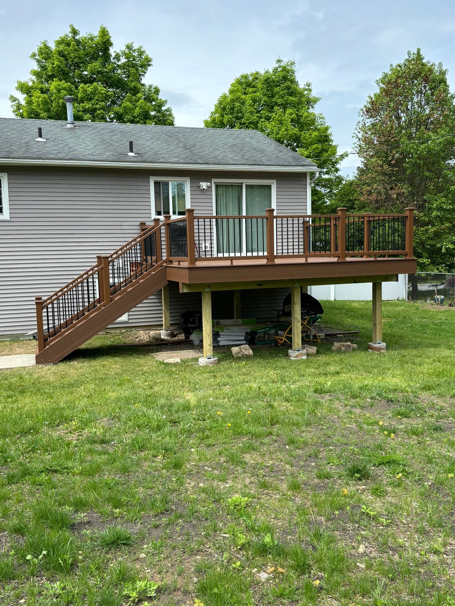 Brown deck with railings, stairs, and a sliding glass door against a gray house; green grass in front.