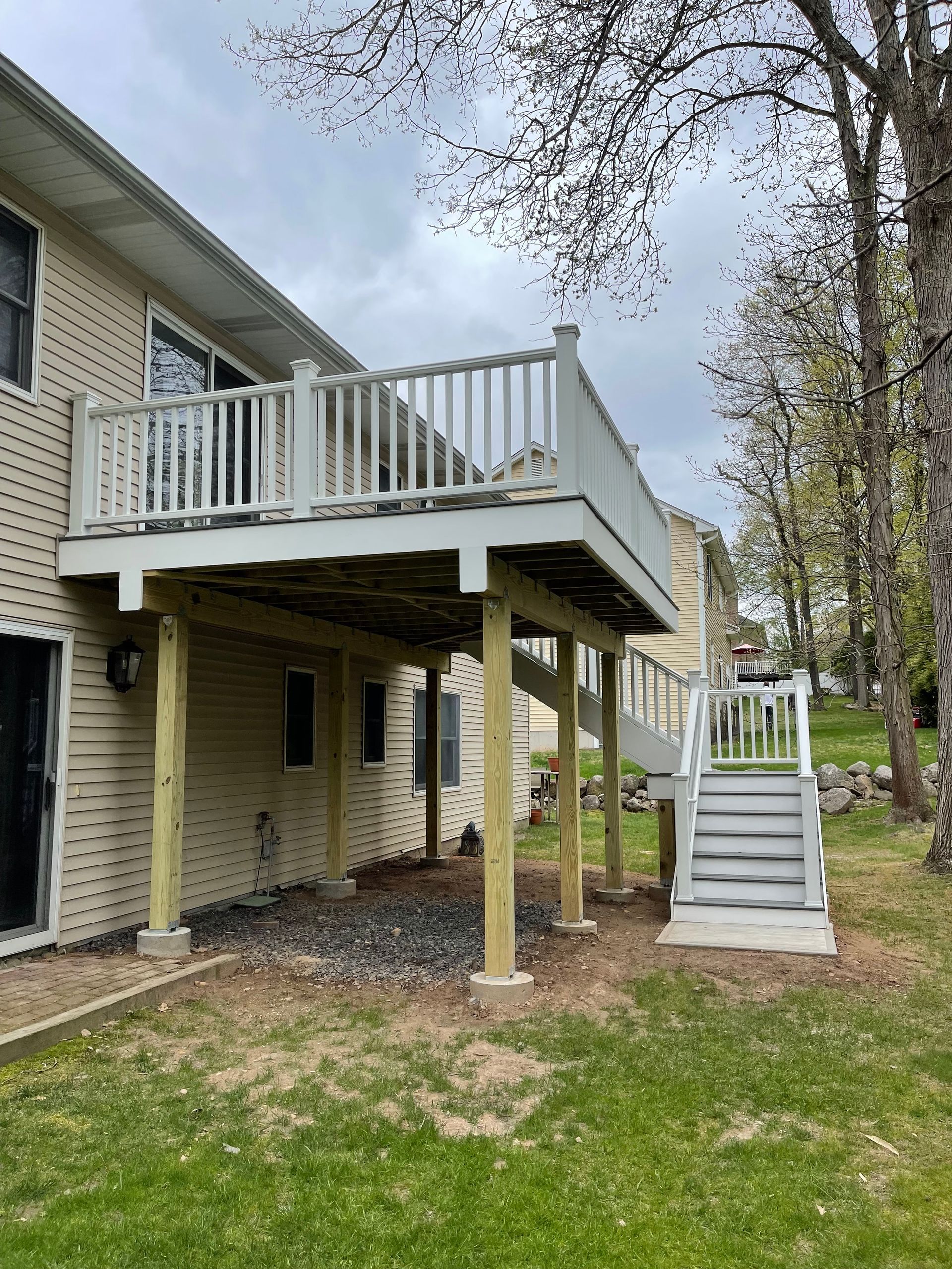 Two-story deck attached to a beige house, with steps leading down to a grassy yard and a shaded area underneath.