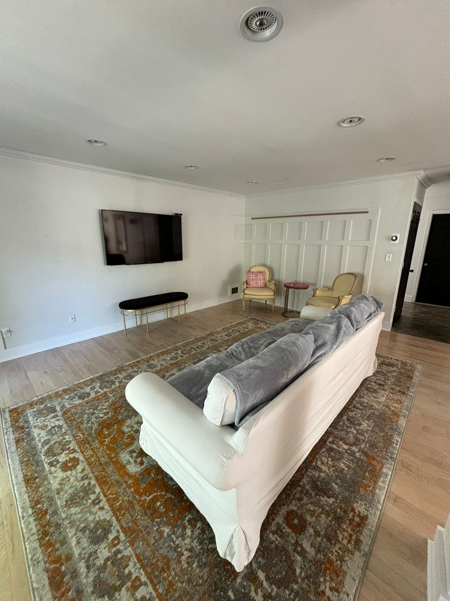 Living room with white sofa, rug, TV, chairs, and wood flooring.