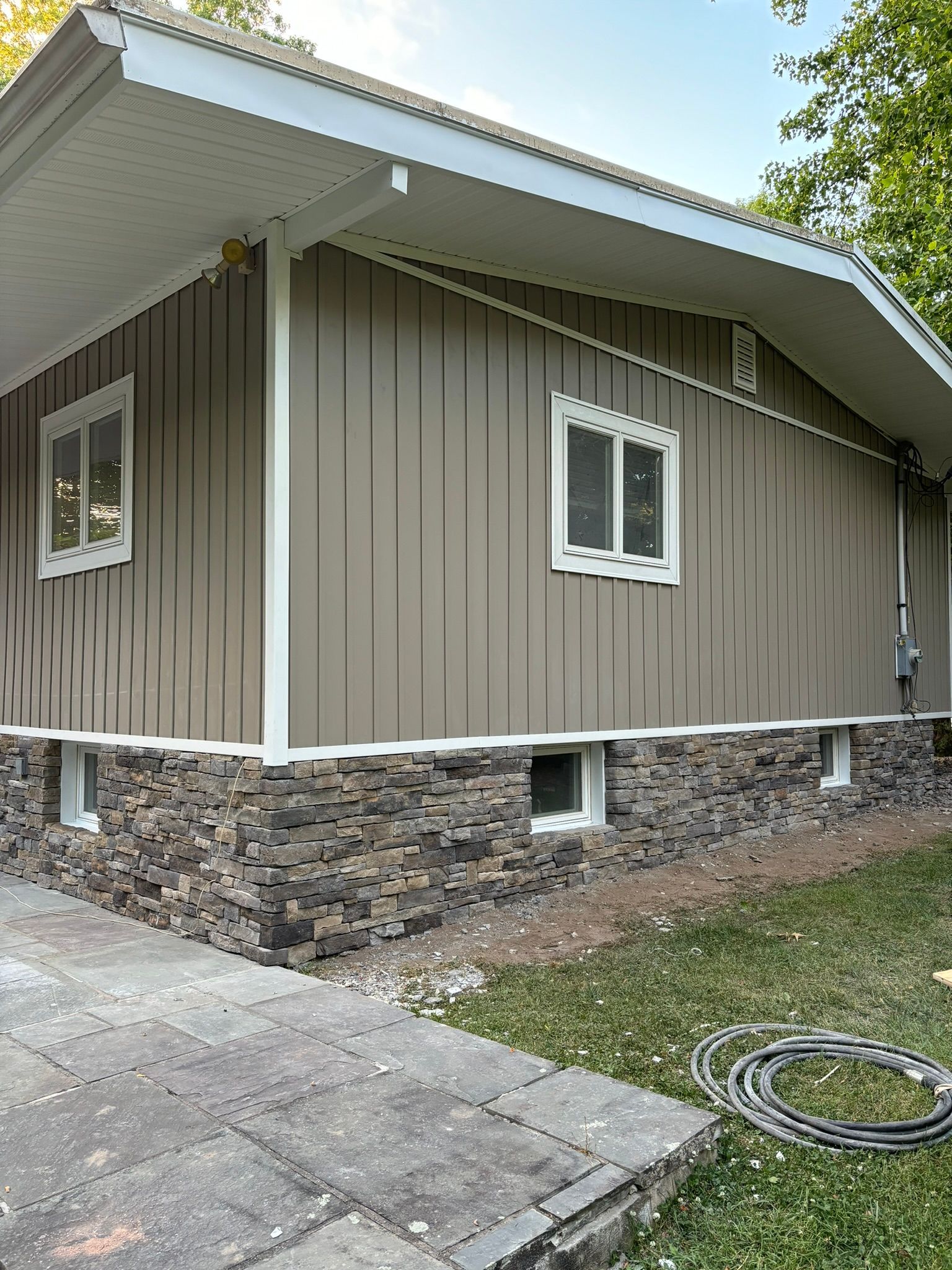 Beige siding and stone veneer on a house, white-framed windows, paved walkway and green lawn.