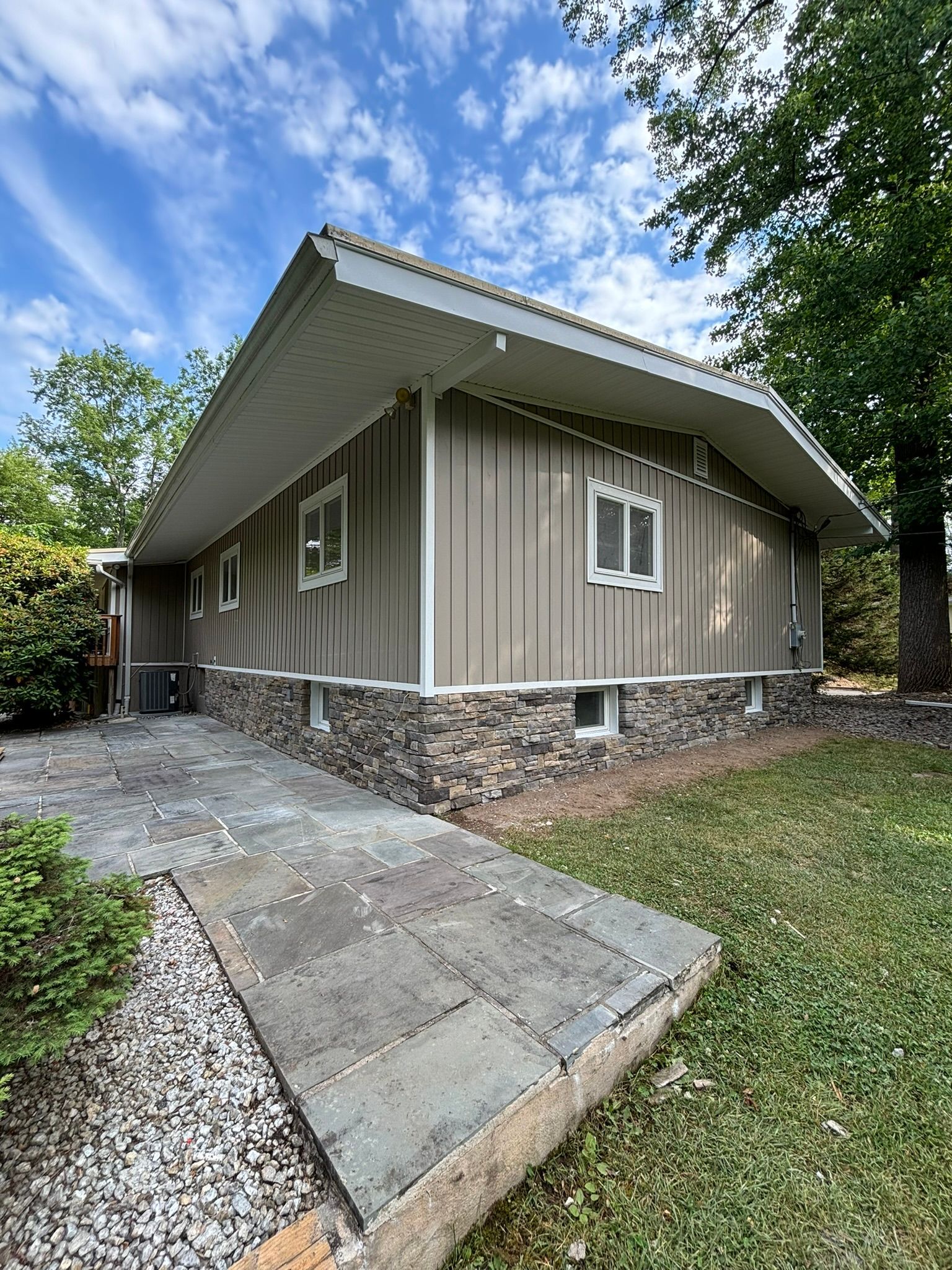 Tan house with stone base and sloped walkway.
