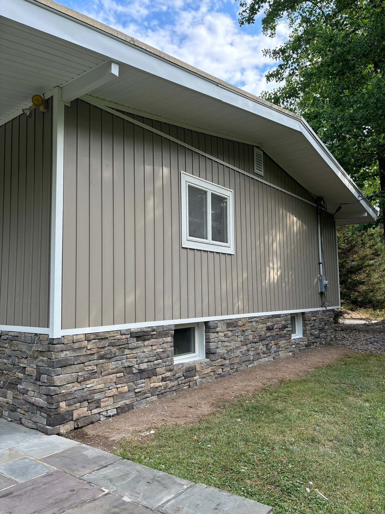 Beige house with stone foundation, vertical siding, white trim, and a small window.