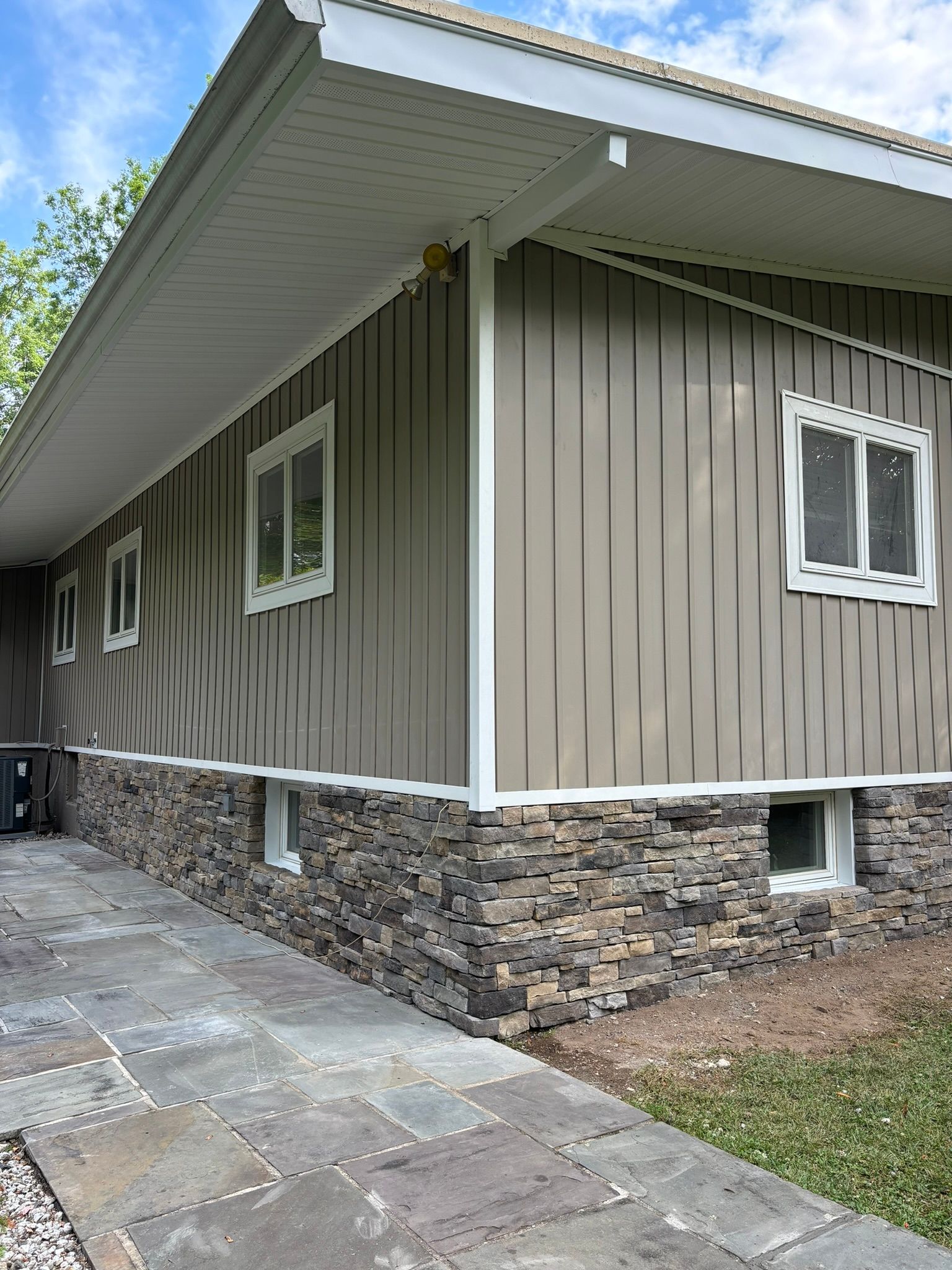 Beige house with stone base and white-framed windows, walkway in front.