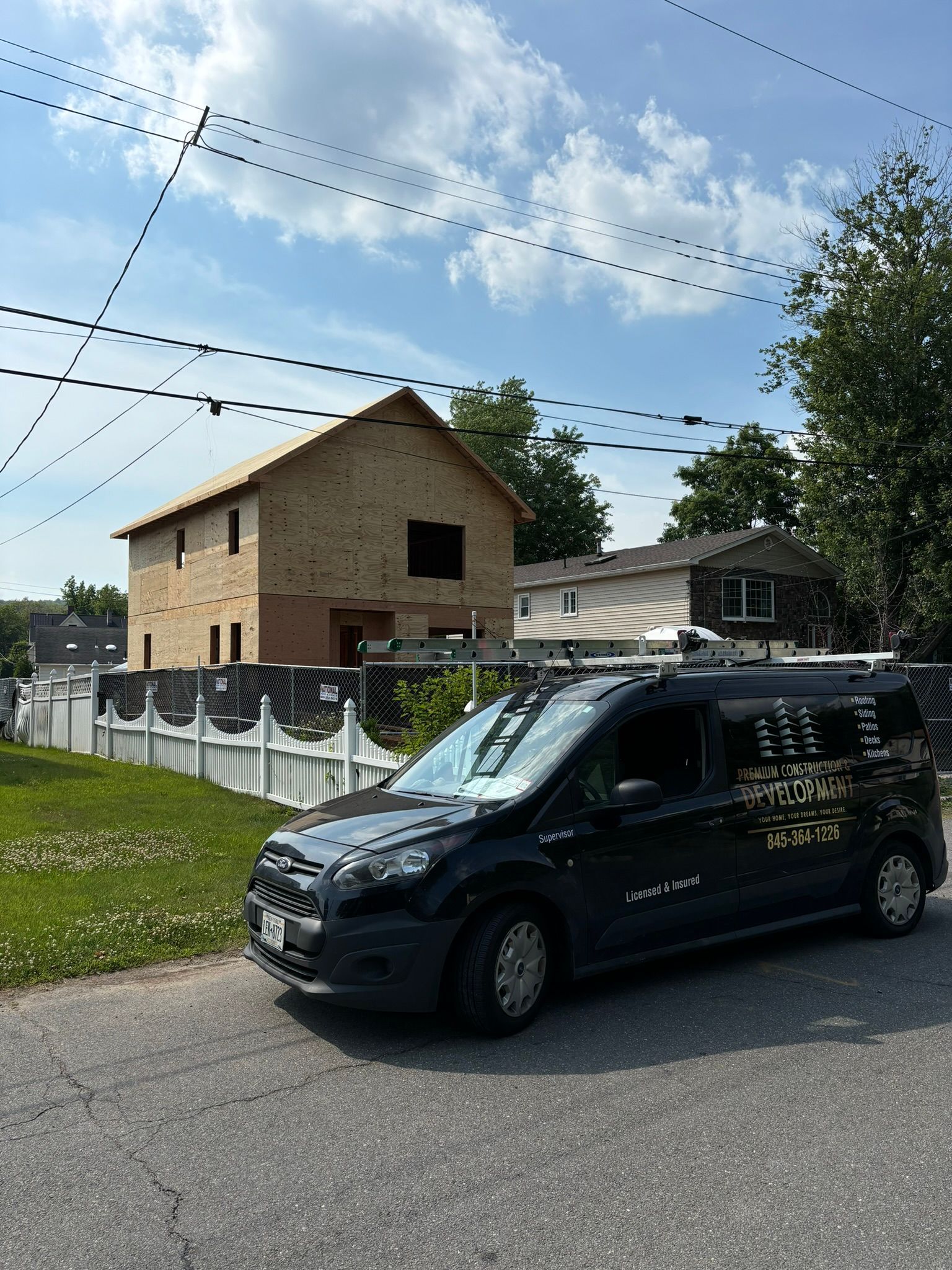 Black van parked on street; house under construction in background. Sunny day.