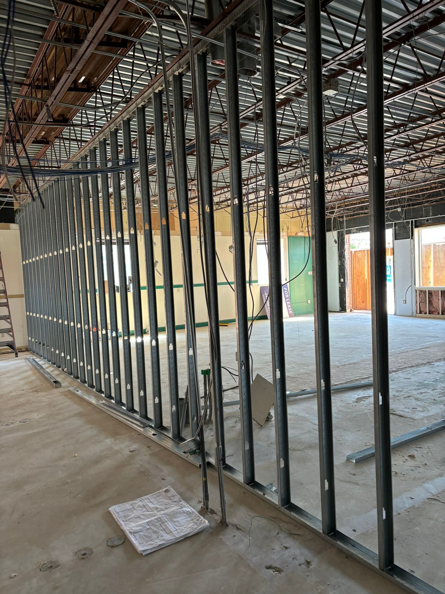 Metal studs frame a construction site's interior wall. Exposed ceiling, concrete floor, open space beyond.