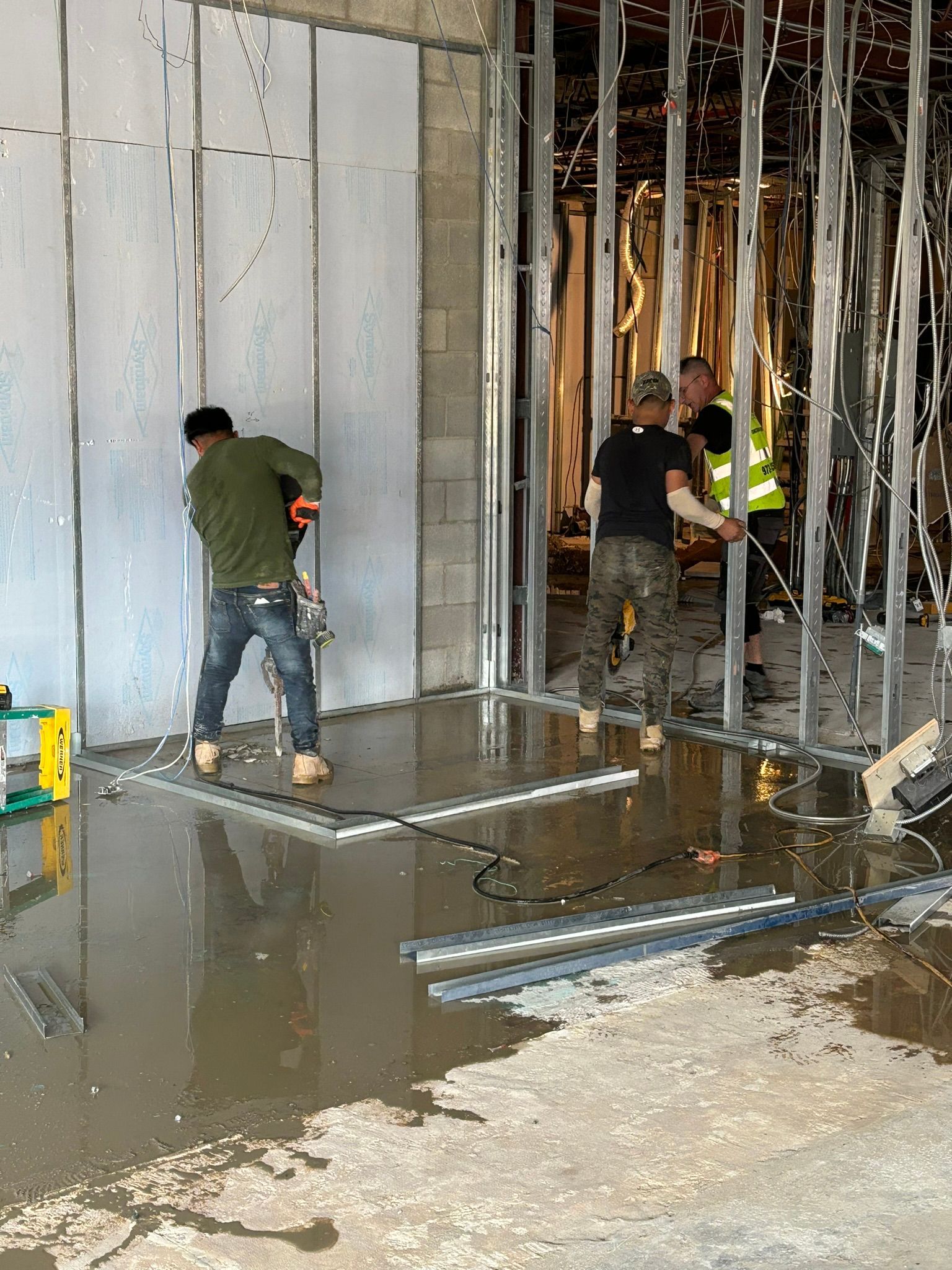 Construction workers installing wall panels. Men using tools in a flooded area with metal framing.