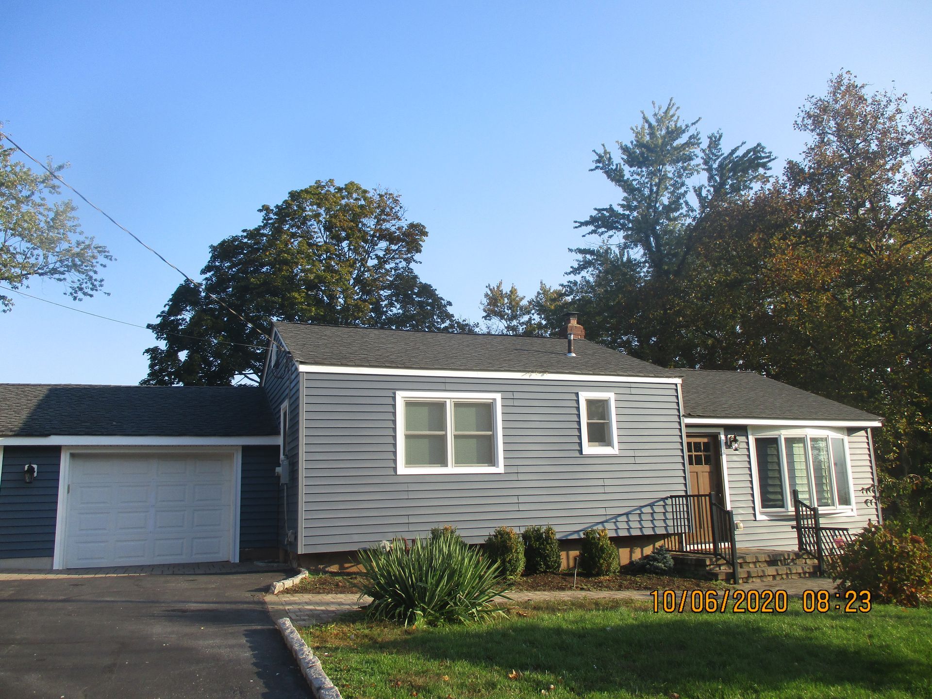 Blue-sided ranch house with attached garage, small bushes, and trees under a clear sky.