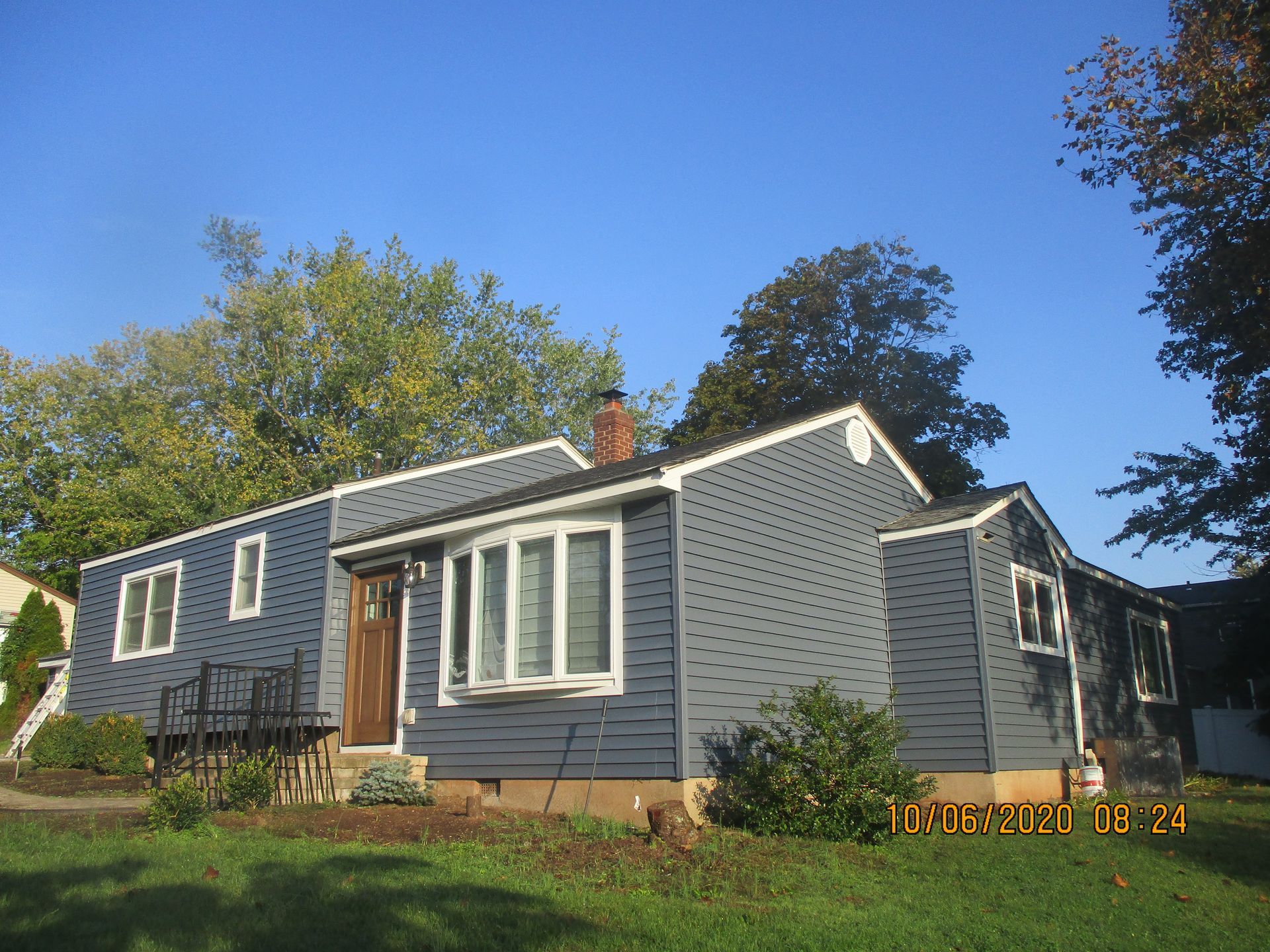 Blue-sided ranch house with white trim, brown door, and green lawn under a blue sky.