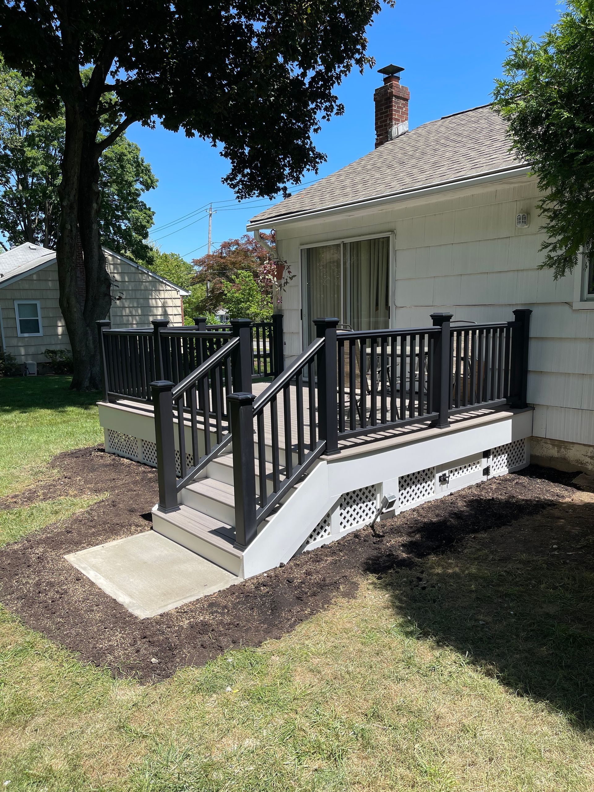 A black-railed deck with stairs in front of a white house. Surrounded by mulch and grass.