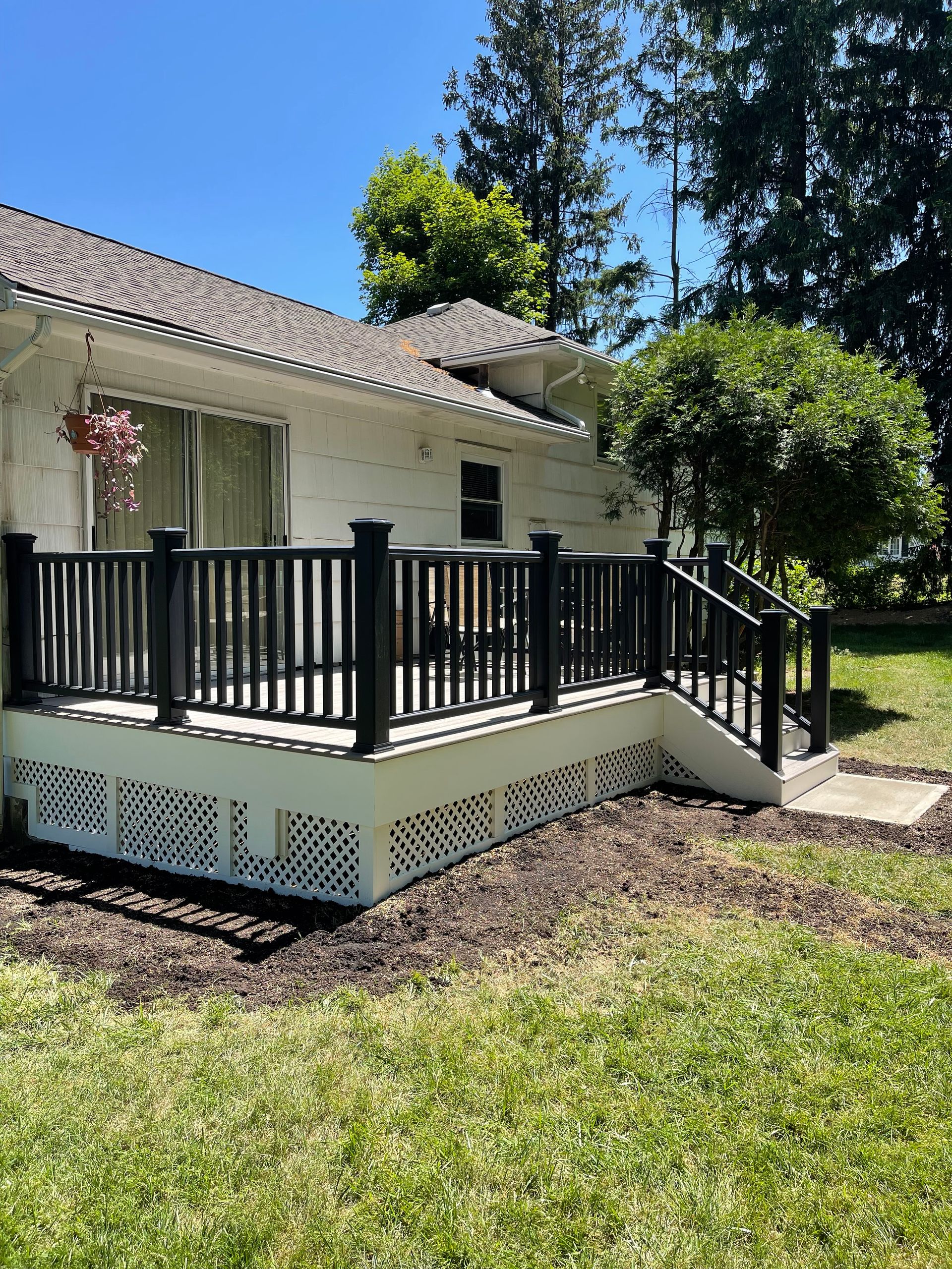 White house with black deck, white lattice base, on green lawn under a blue sky.