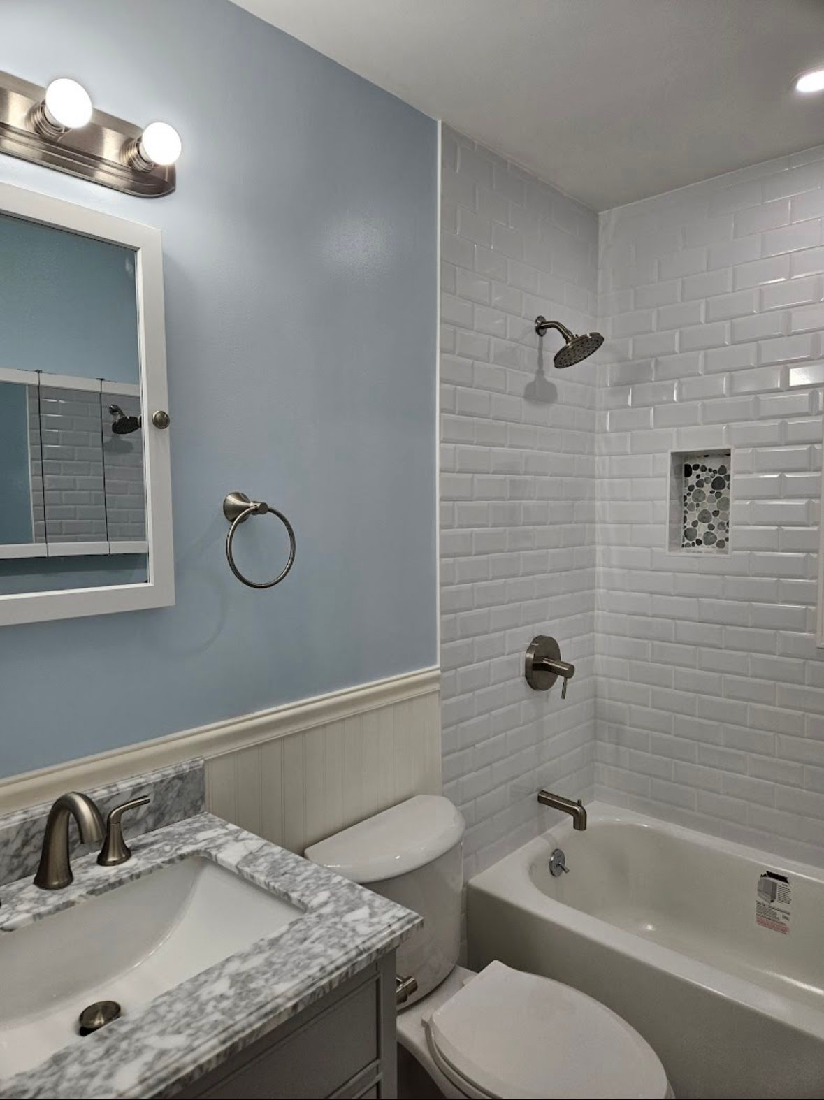 Bathroom with blue walls, white subway tile shower, white tub, and gray marble vanity.