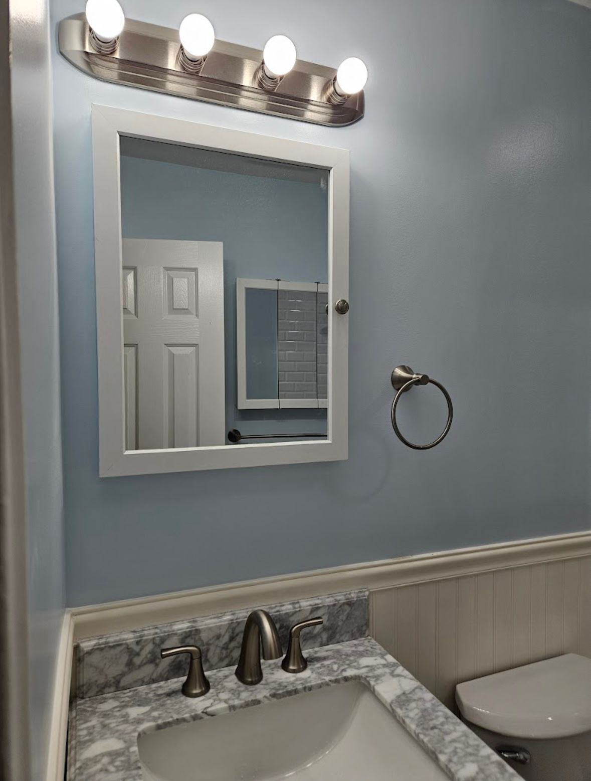 Bathroom with light blue walls, white framed mirror, and brushed nickel fixtures.