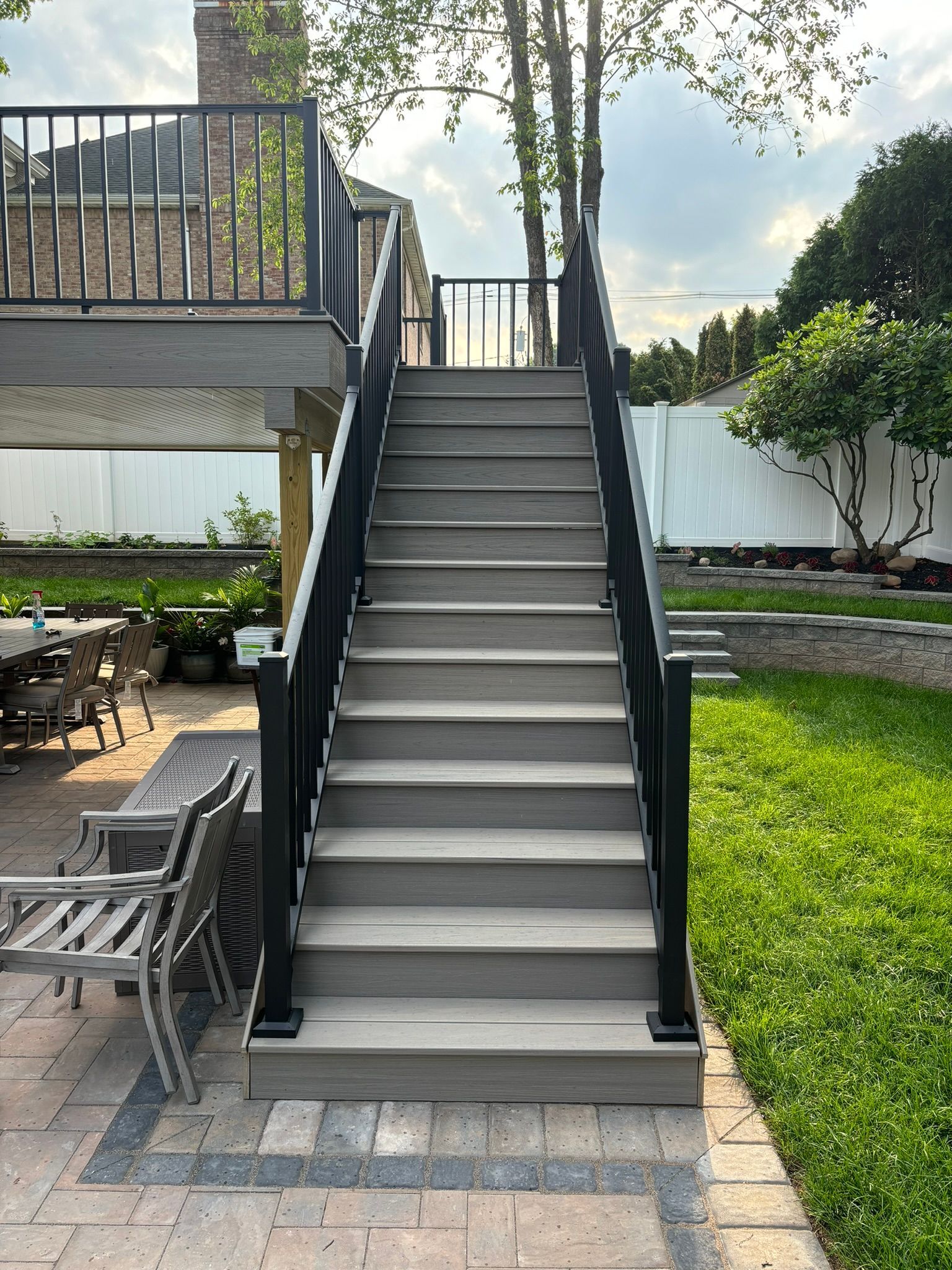 Gray staircase with black railing leads up to a deck. Outdoor setting with patio furniture.