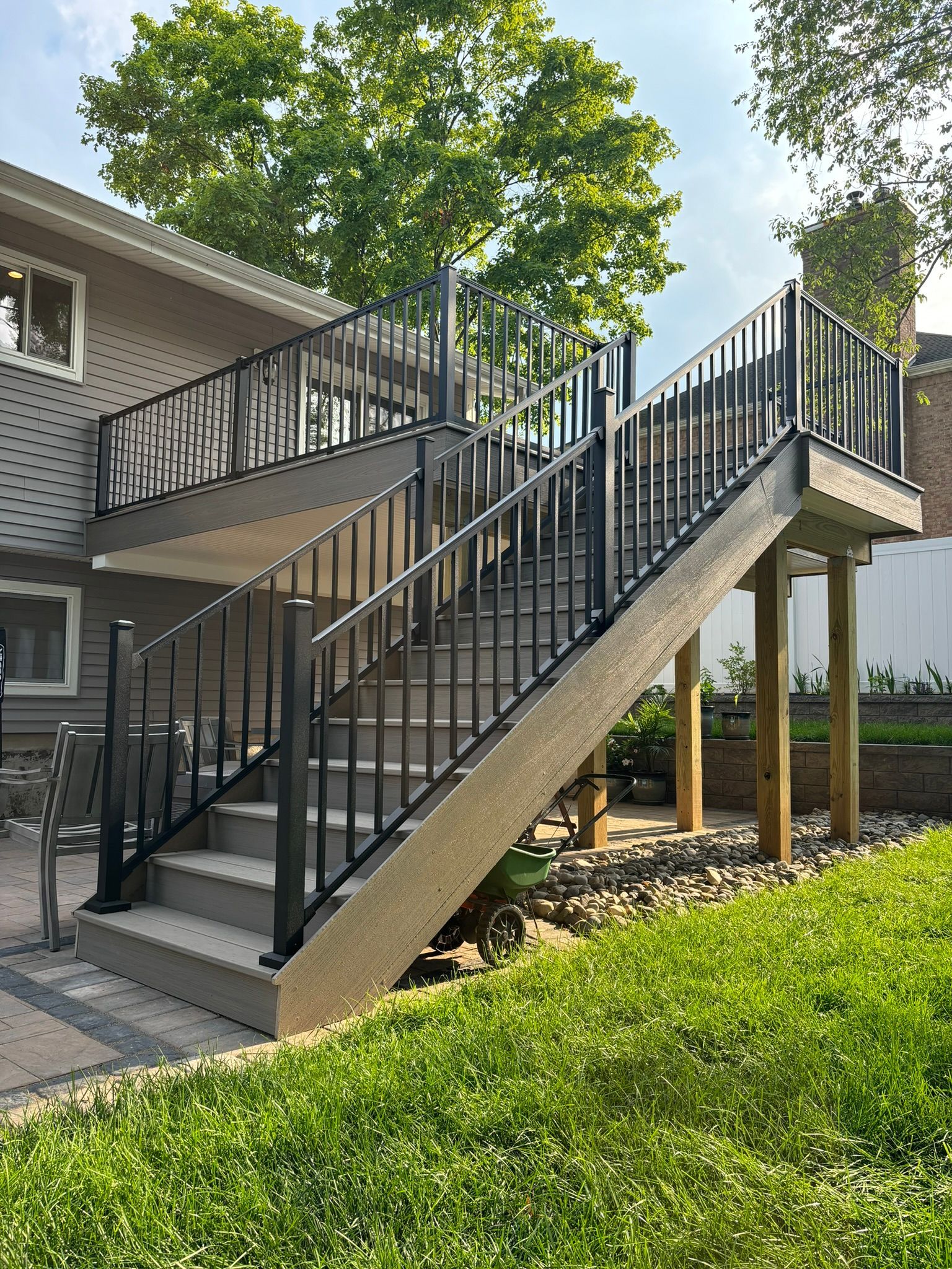 Two-story deck with stairs and black railings against a house. Green grass and trees surround it.