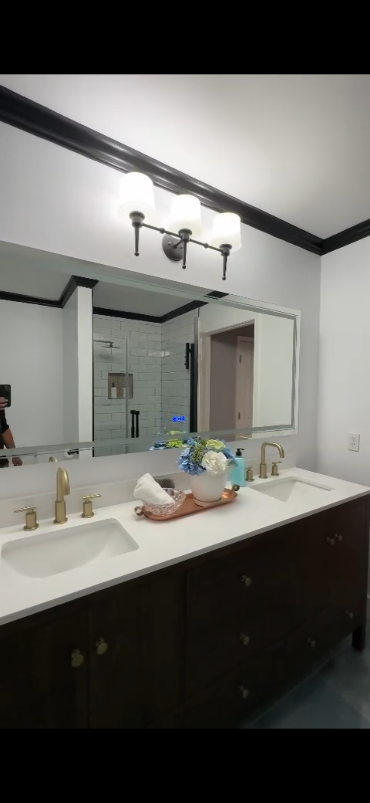 Bathroom with a dark brown vanity, white countertop, and gold fixtures. A mirror and overhead lights are present.