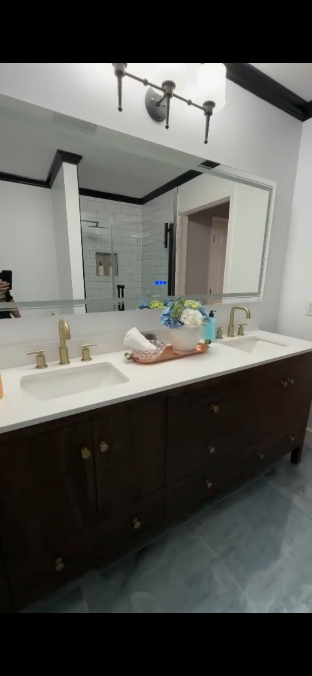 Bathroom with a dark brown vanity, white countertop, and large mirror. Brass fixtures and blue floor.