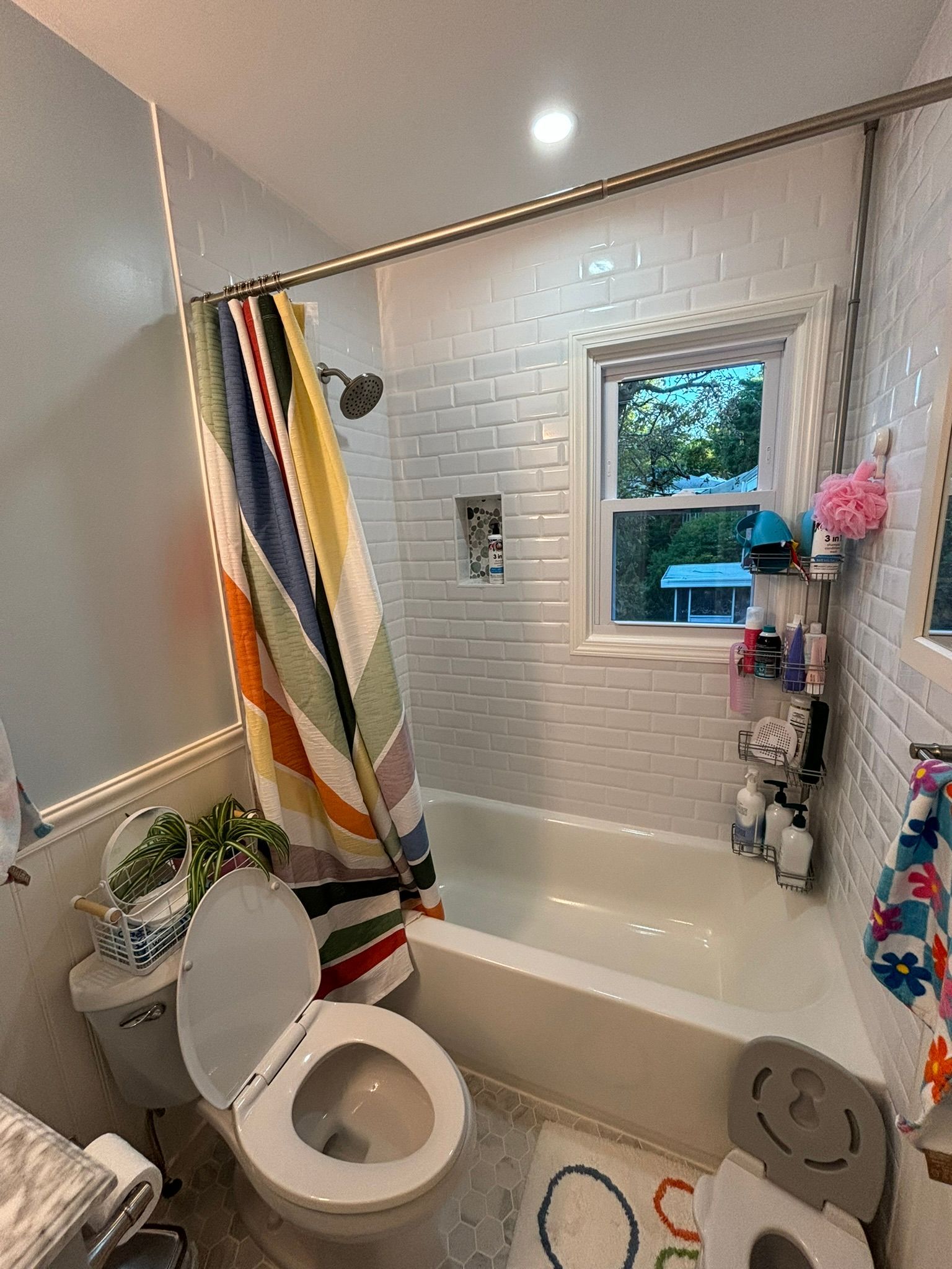 Bathroom with white tile, a bathtub, toilet, shower curtain, and a window.