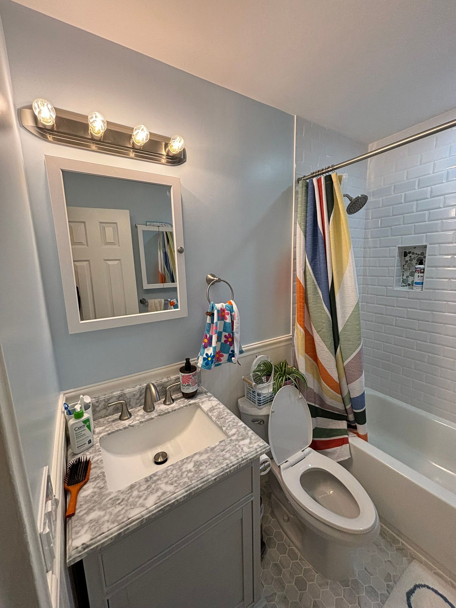 Bathroom with light blue walls, gray vanity with sink, toilet, and patterned shower curtain.