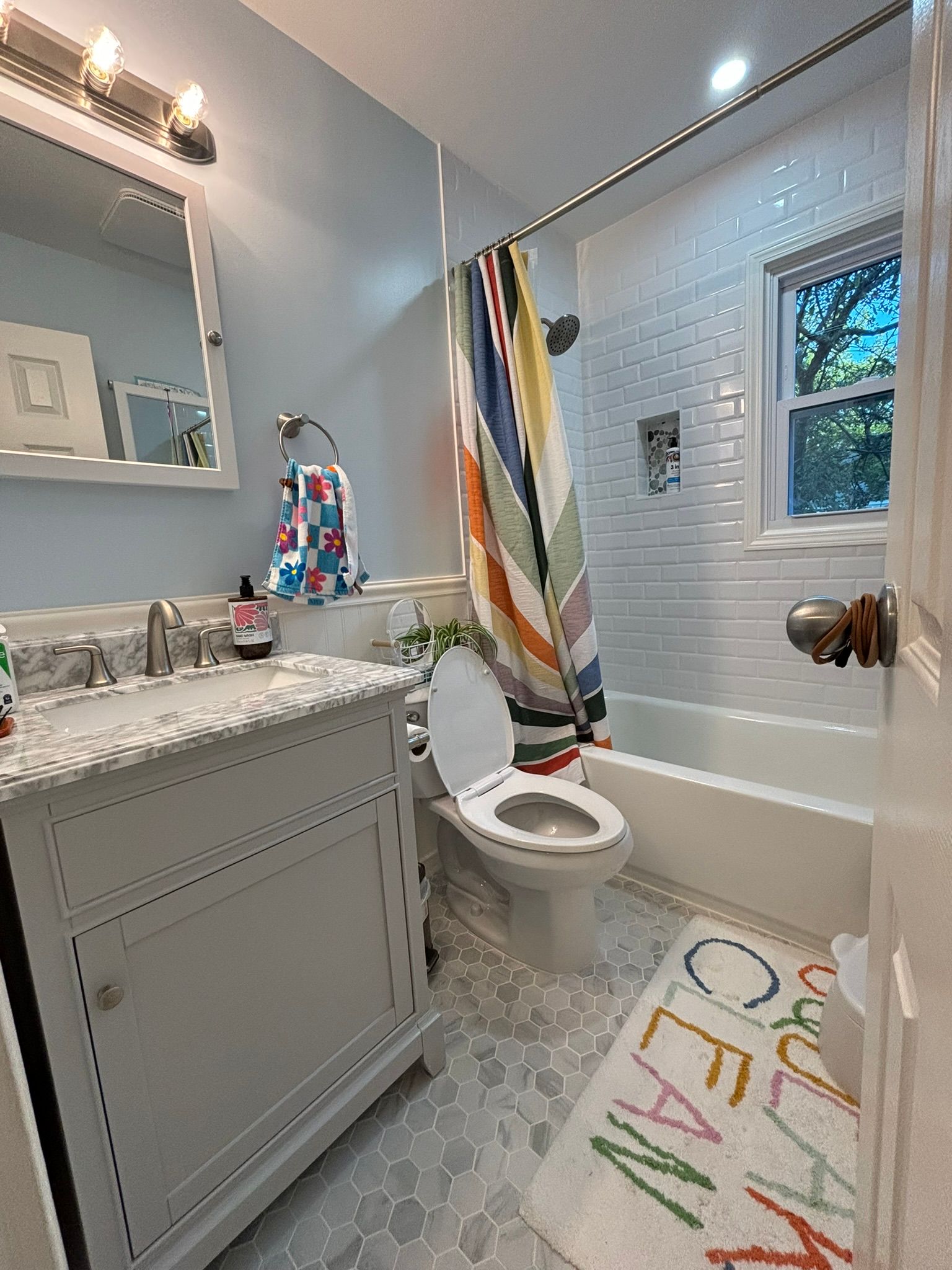 Bathroom with light blue walls, white vanity, and patterned shower curtain.