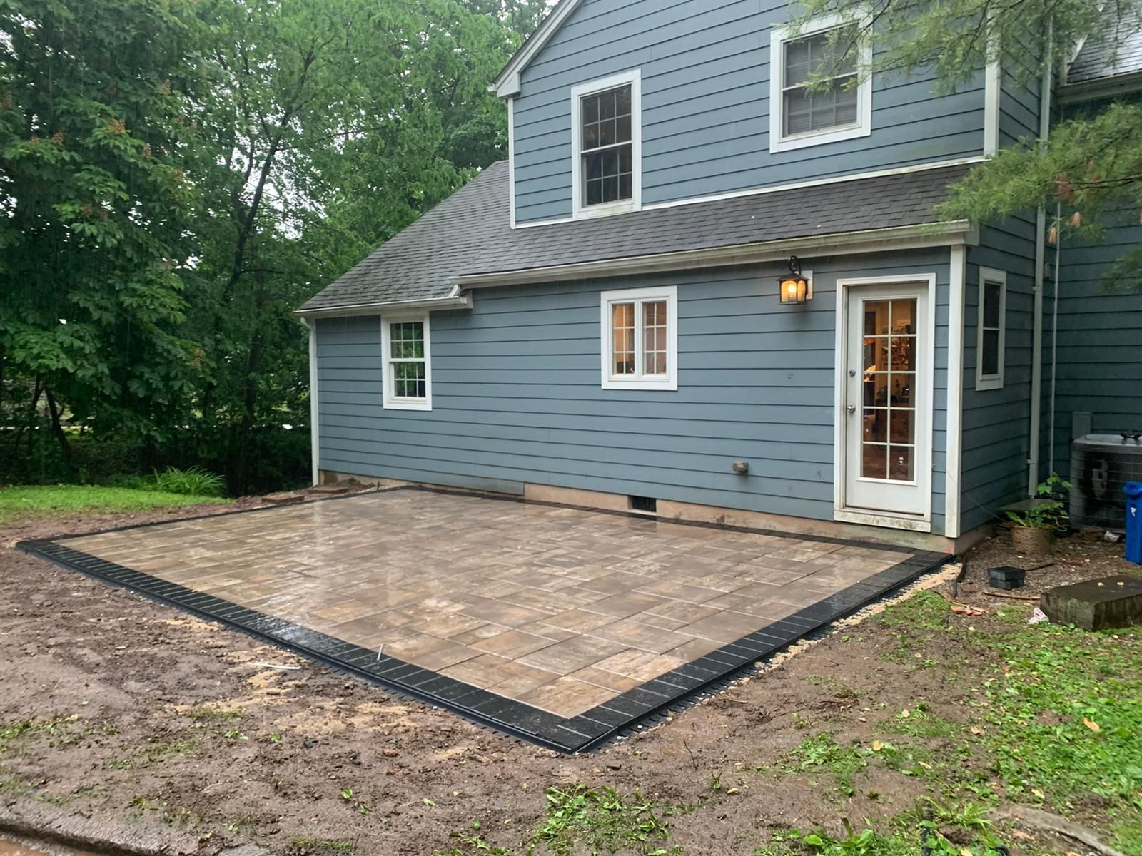 A backyard patio with a blue house in the background and a black border.
