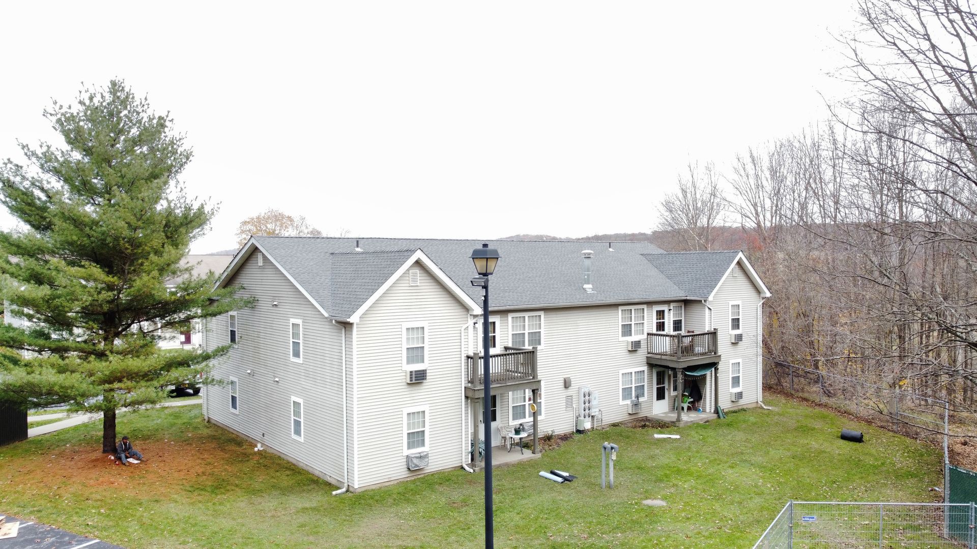 Two-story apartment building with light siding, gray roof, and small balconies on a grassy lawn.