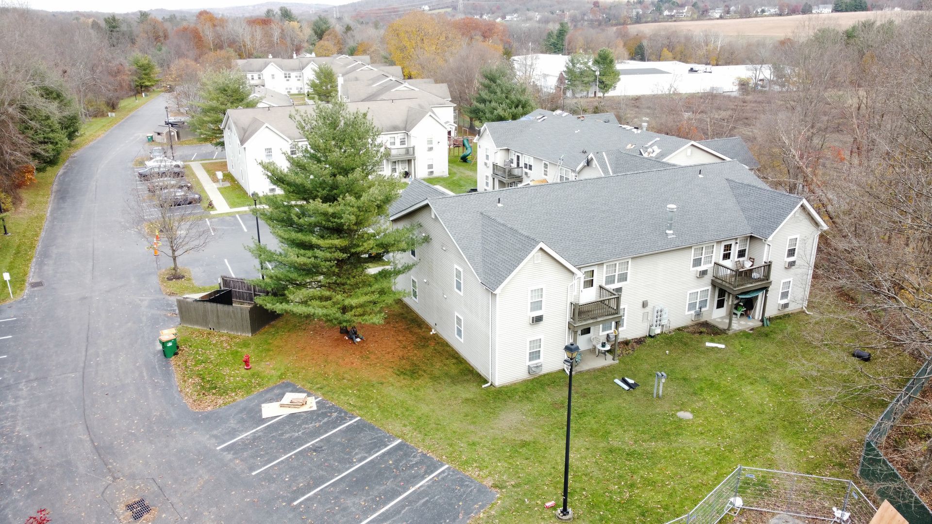 Apartment buildings with gray roofs and beige siding, surrounded by a parking lot and grass, on a cloudy day.