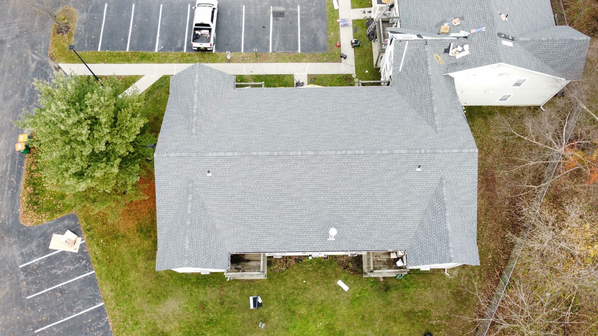 Aerial view of a gray roofed building, surrounded by green grass and a parking lot with a few parked vehicles.