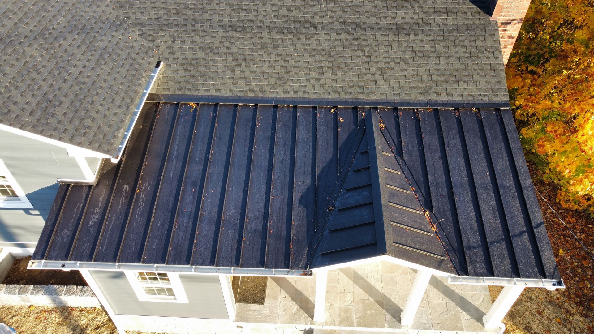 Overhead view of a house with a dark gray metal roof.  Gray siding with white trim. Autumn trees.