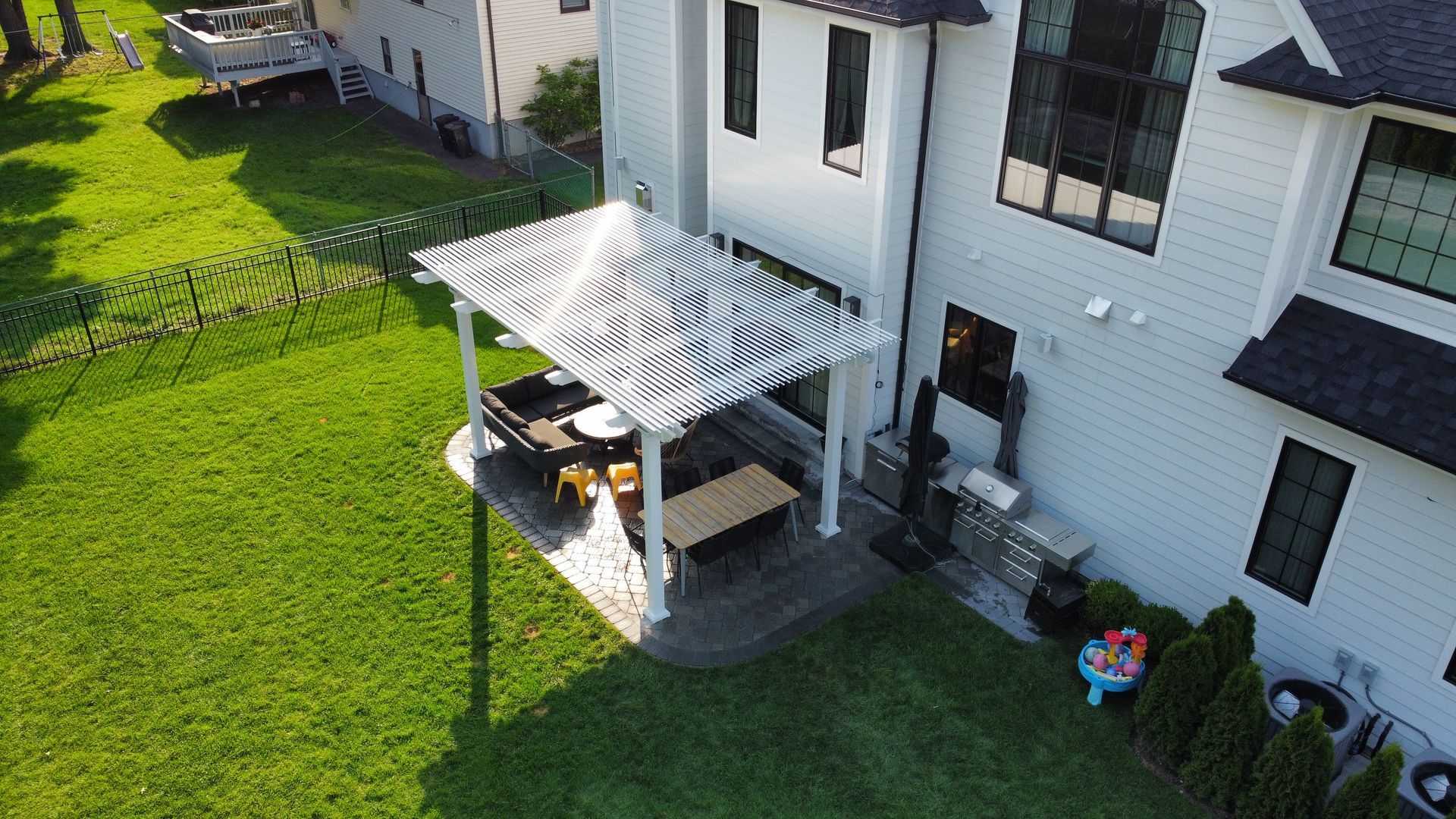 Backyard with white house, patio, pergola, and green lawn.