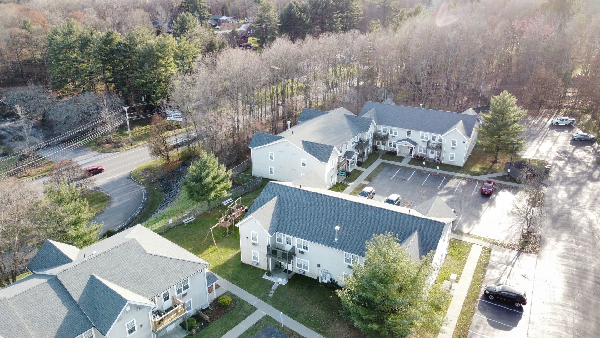 Aerial view of apartment buildings surrounded by trees and a parking lot.