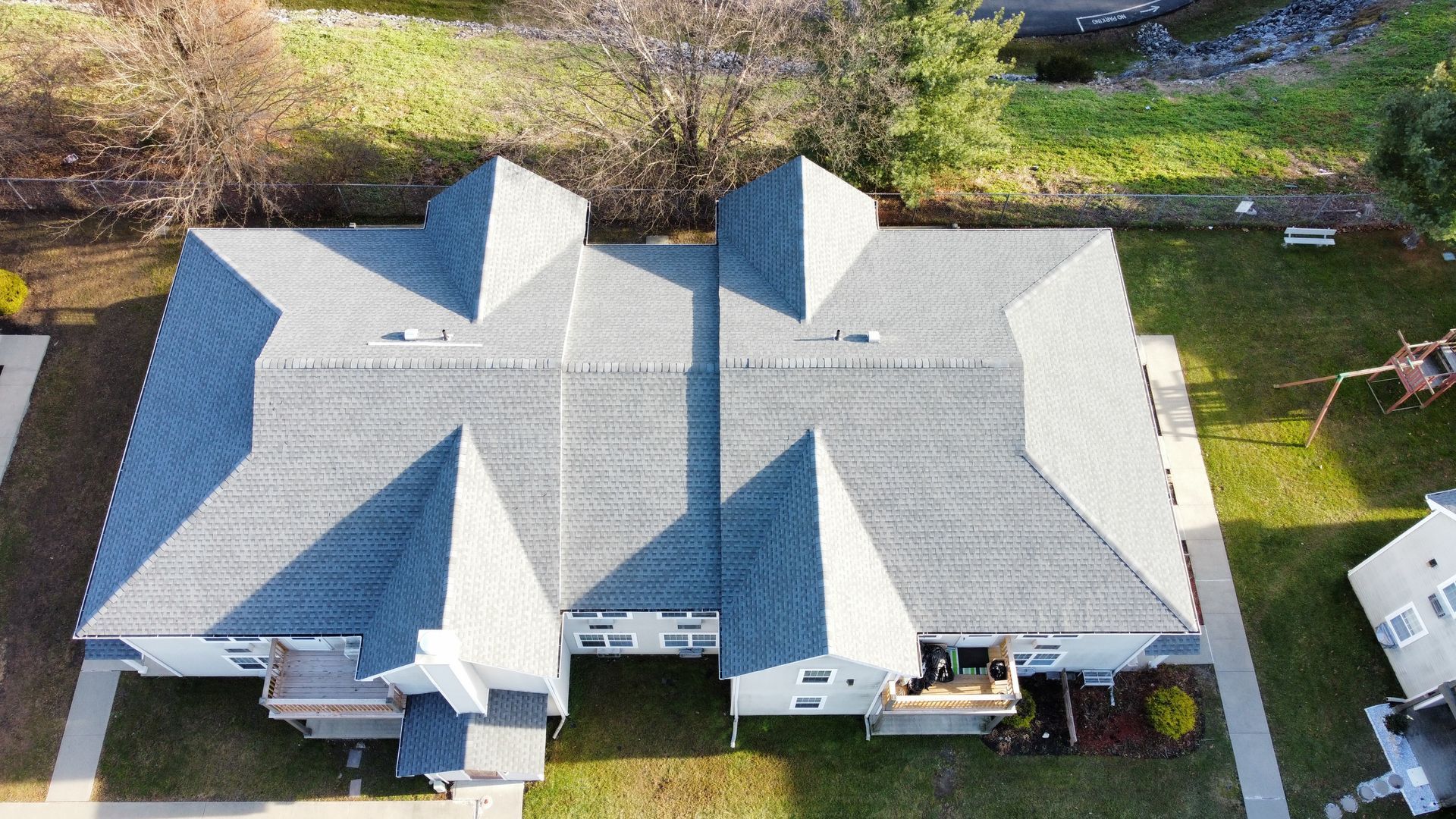 Aerial view of two attached houses with gray roofs and small lawns.