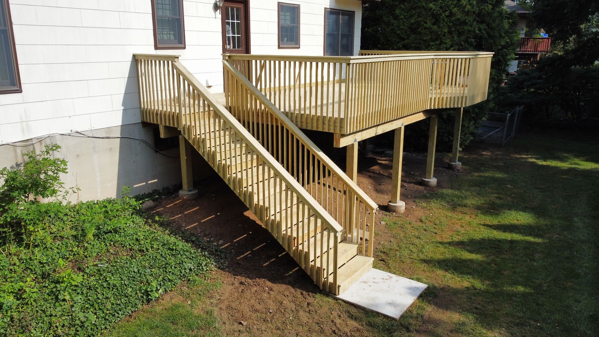 Wooden deck with stairs leading to a house, supported by posts, in a grassy yard.