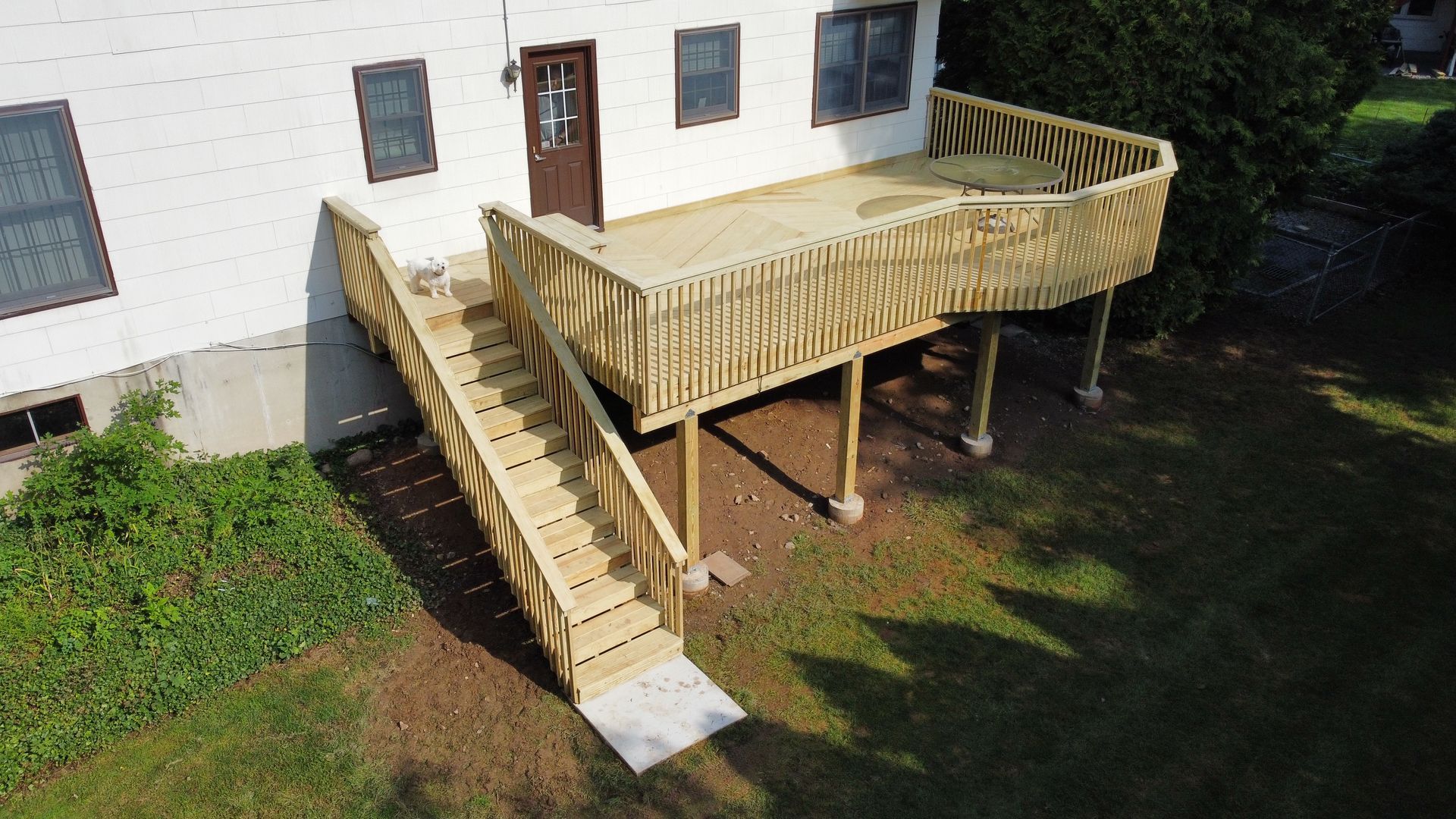 Wooden deck with stairs leading down to a concrete pad, attached to a white house.