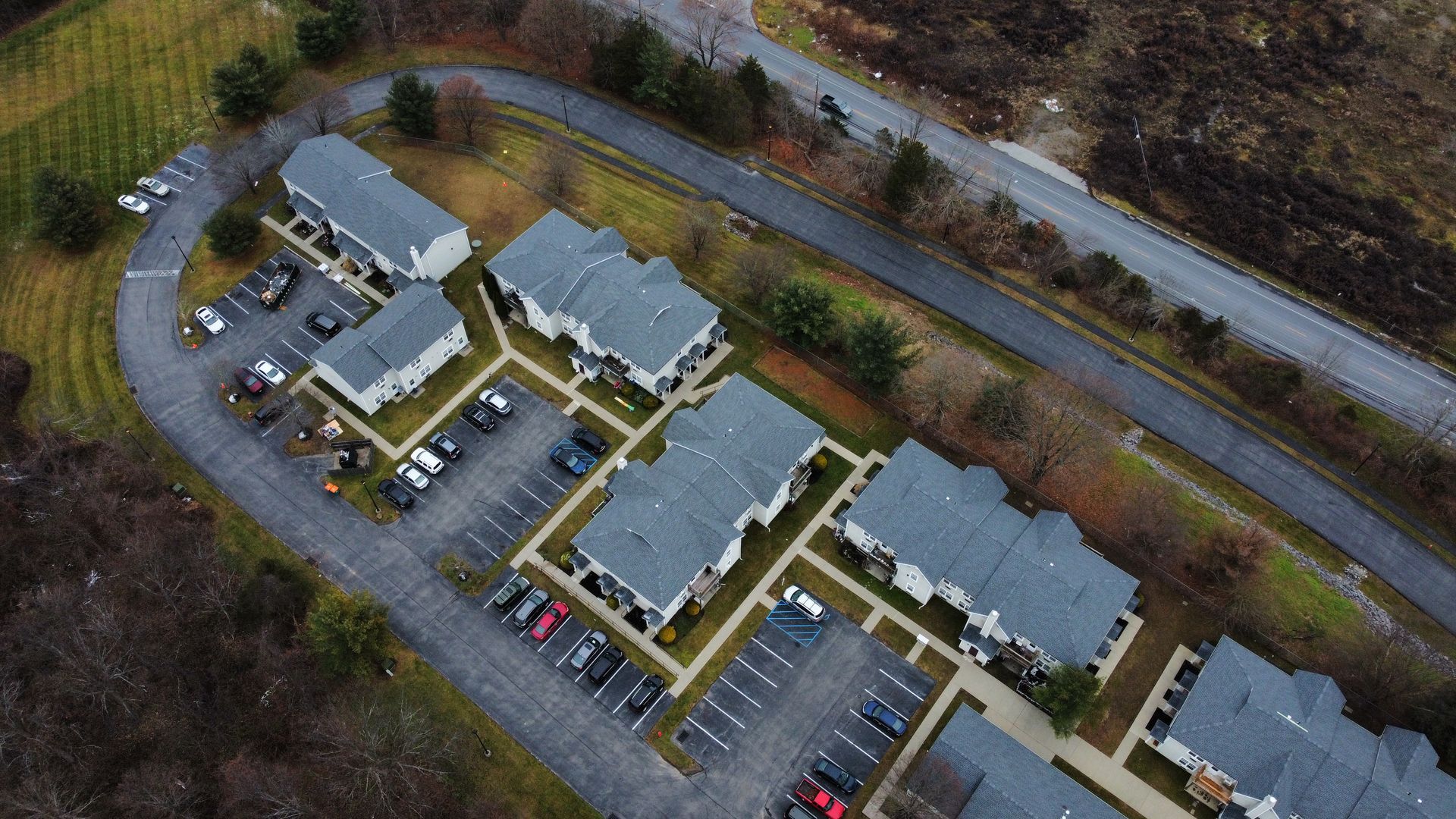 Aerial view of apartment complex with gray roofs, parking lots, and winding road.
