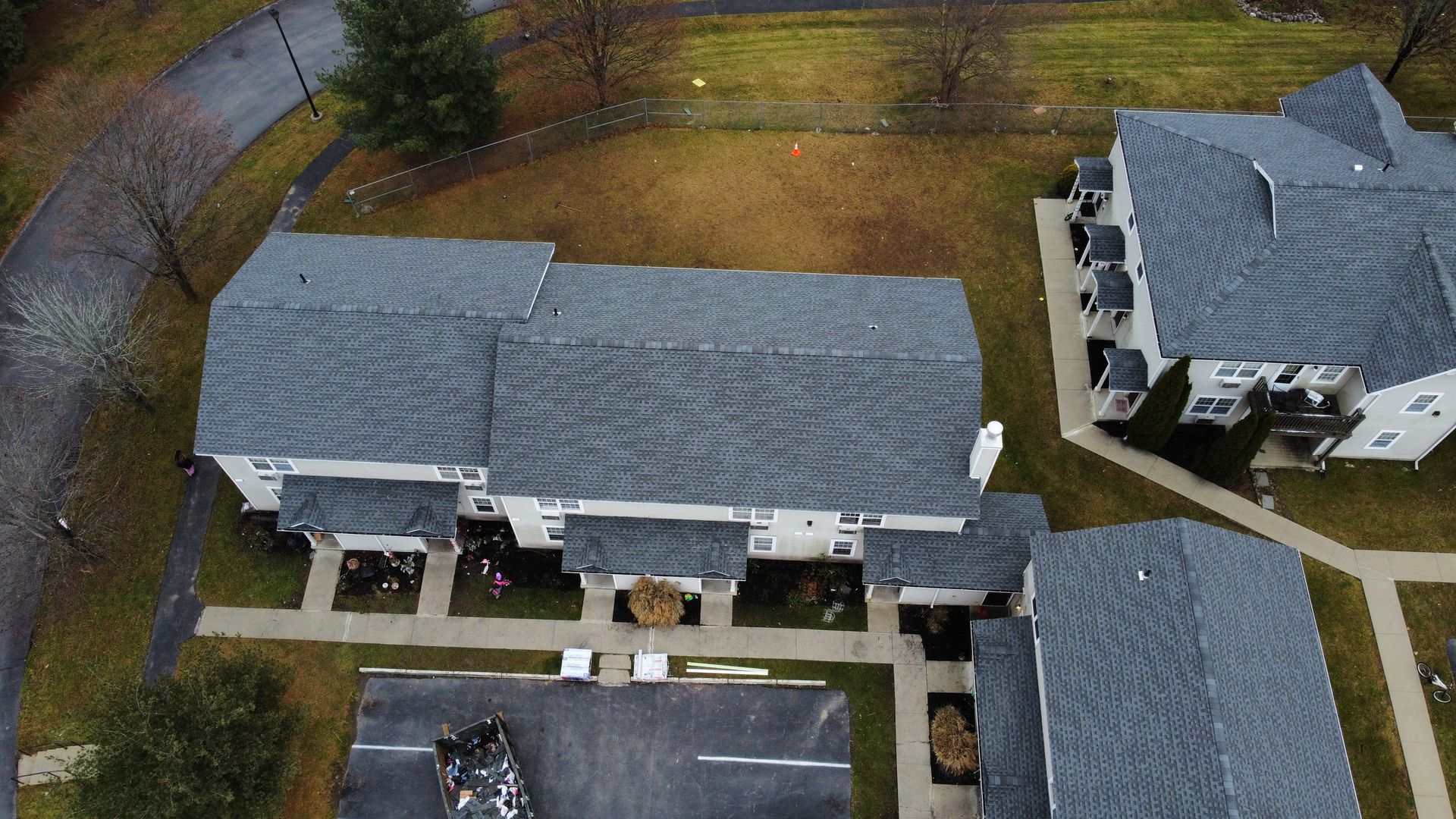 Overhead view of multi-unit residential buildings with gray roofs and surrounding green space, on an overcast day.