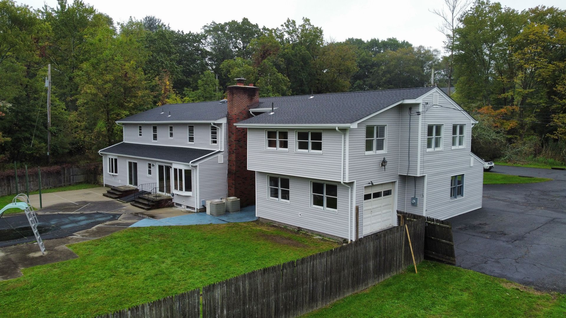 Gray two-story house with a brick chimney, a white garage door, and a green lawn.