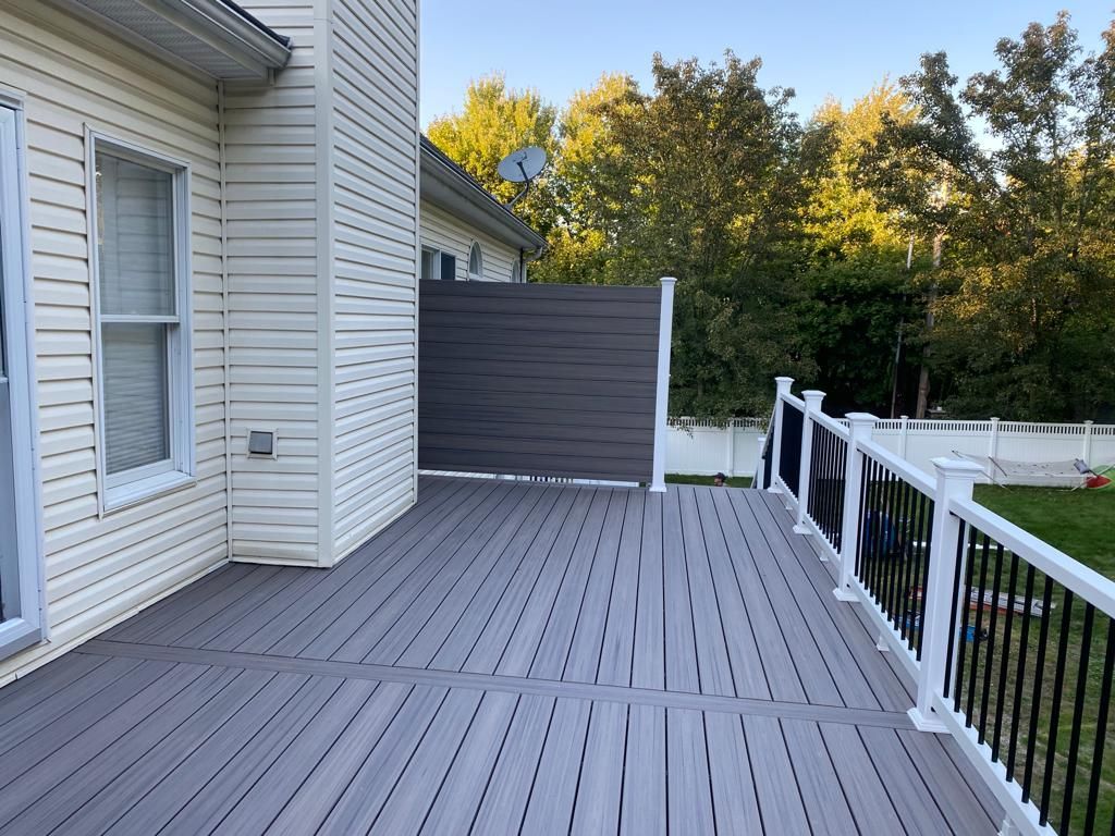 Gray composite deck with white railings, and a privacy screen next to a house.