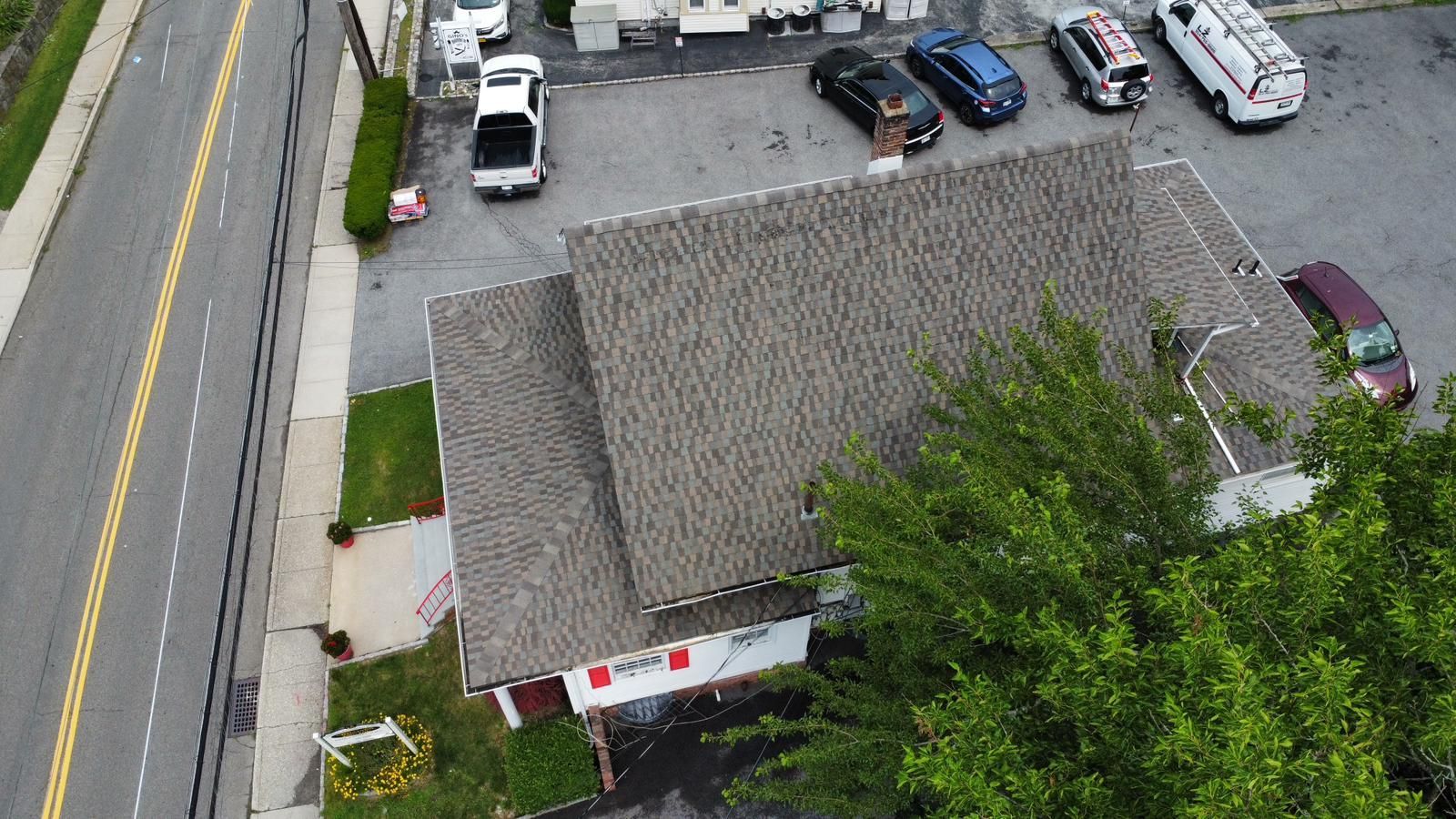 Overhead view of a building with a gray roof, vehicles parked in a lot, and a tree on the right.