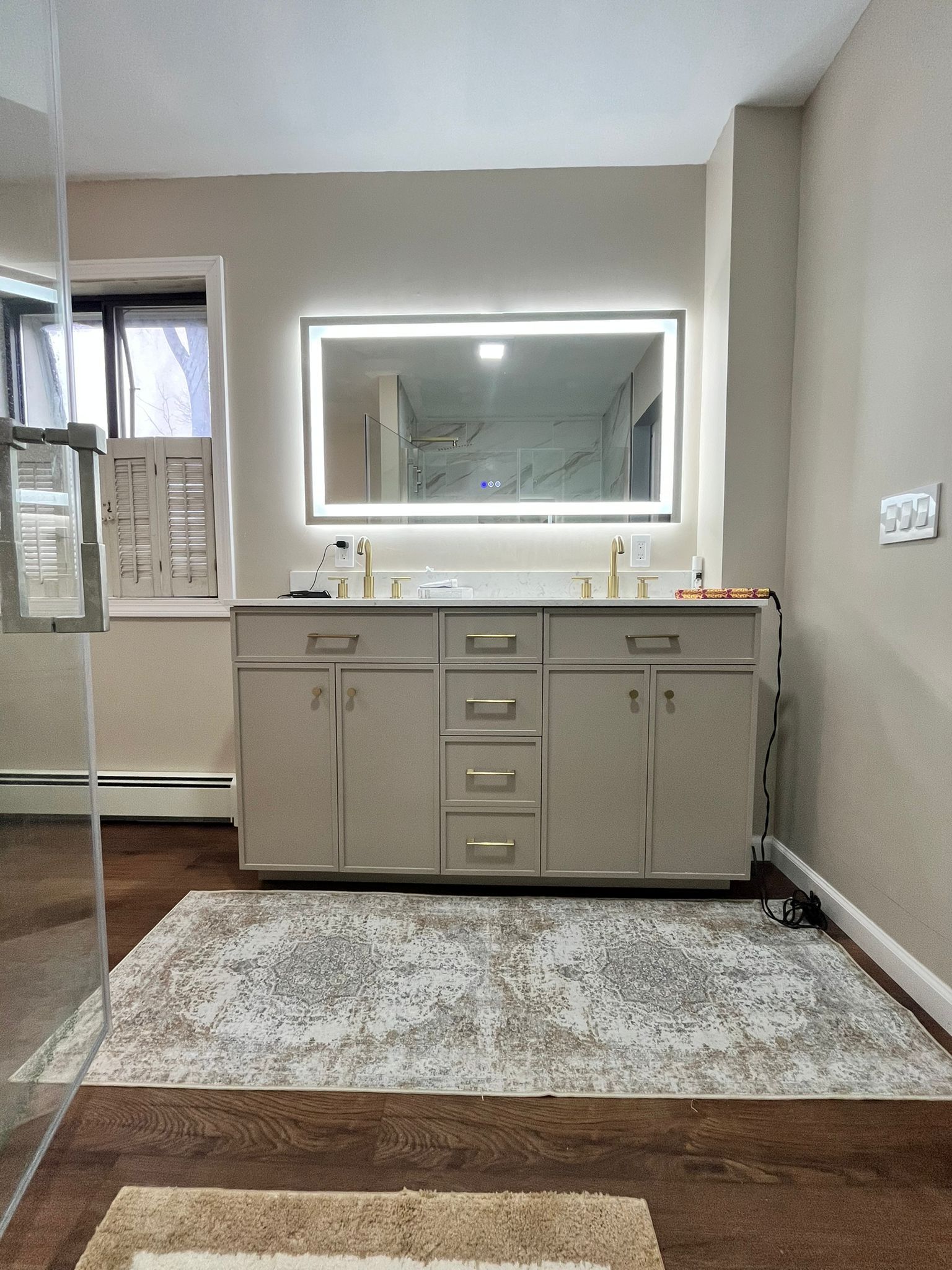 Bathroom with beige vanity, illuminated mirror, and patterned rug.