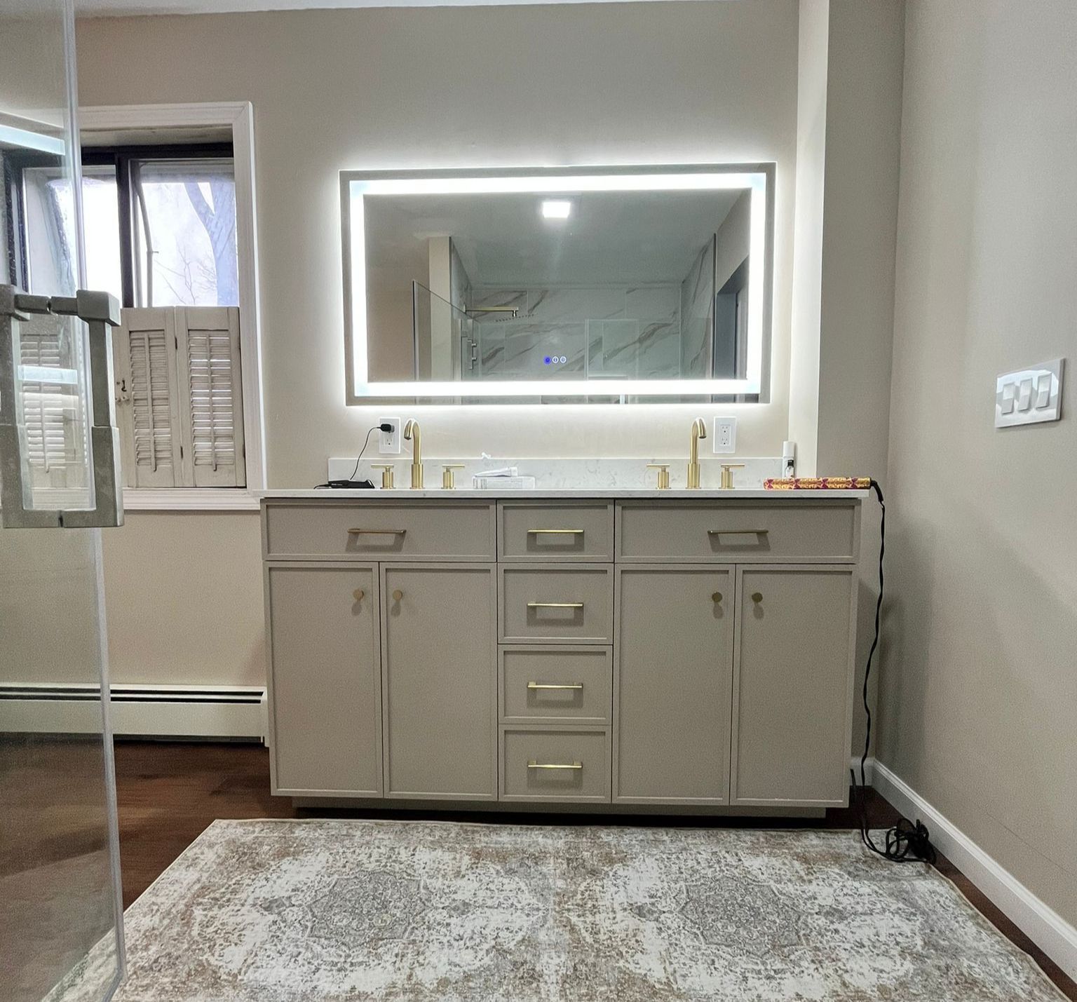 Bathroom with a vanity, large mirror with lights, and a decorative rug.