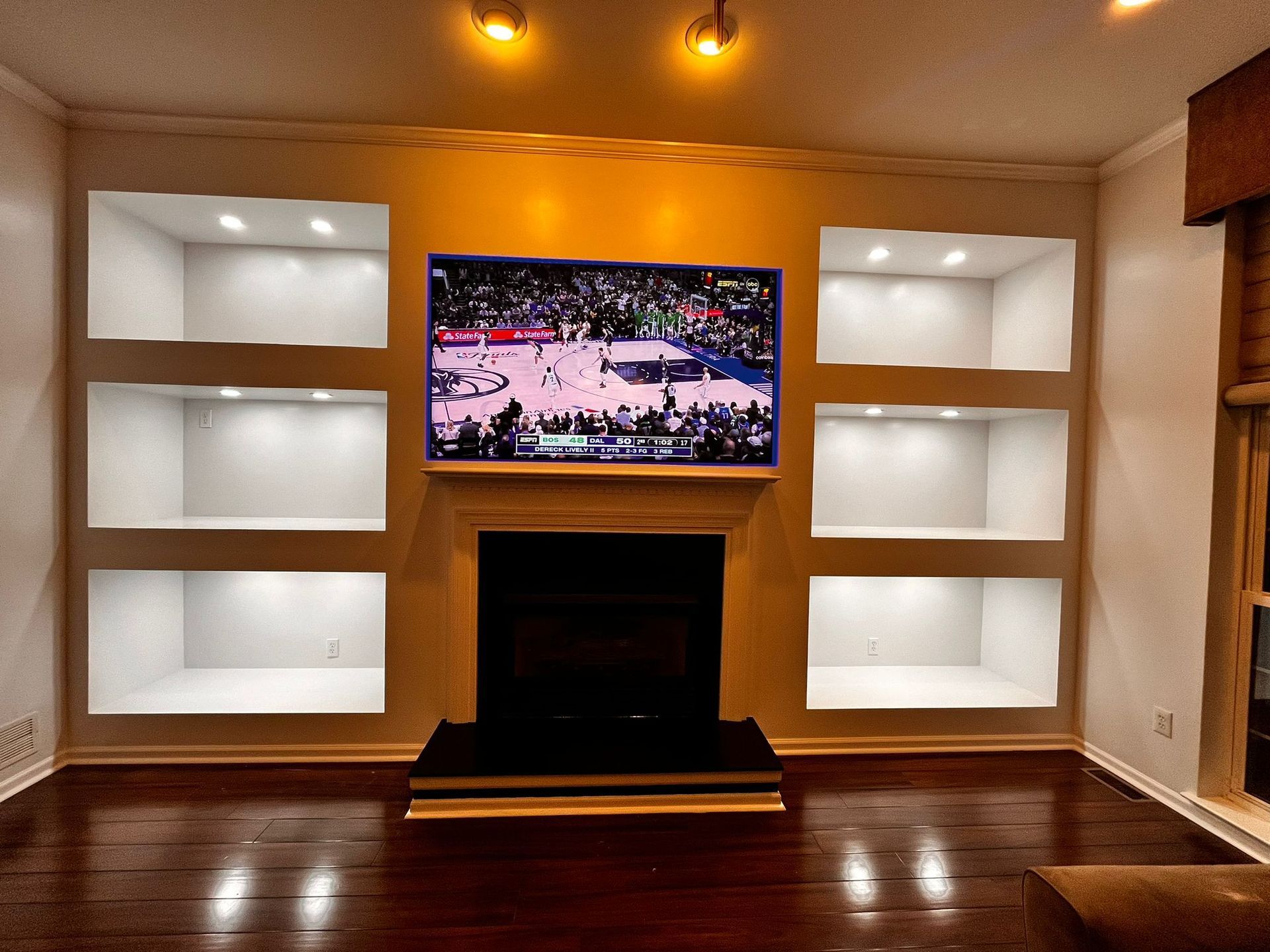 Living room with recessed shelves flanking a fireplace and TV. Shelves are lit with spotlights, and the floor is wood.