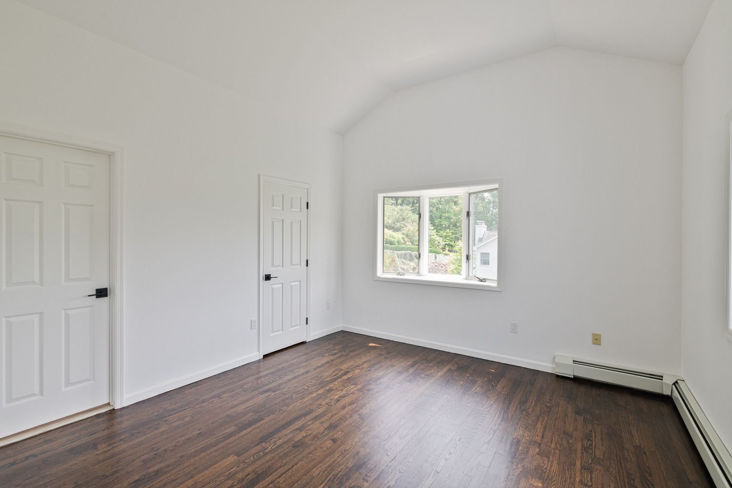 Empty room with hardwood floors, white walls, two doors, and a window.