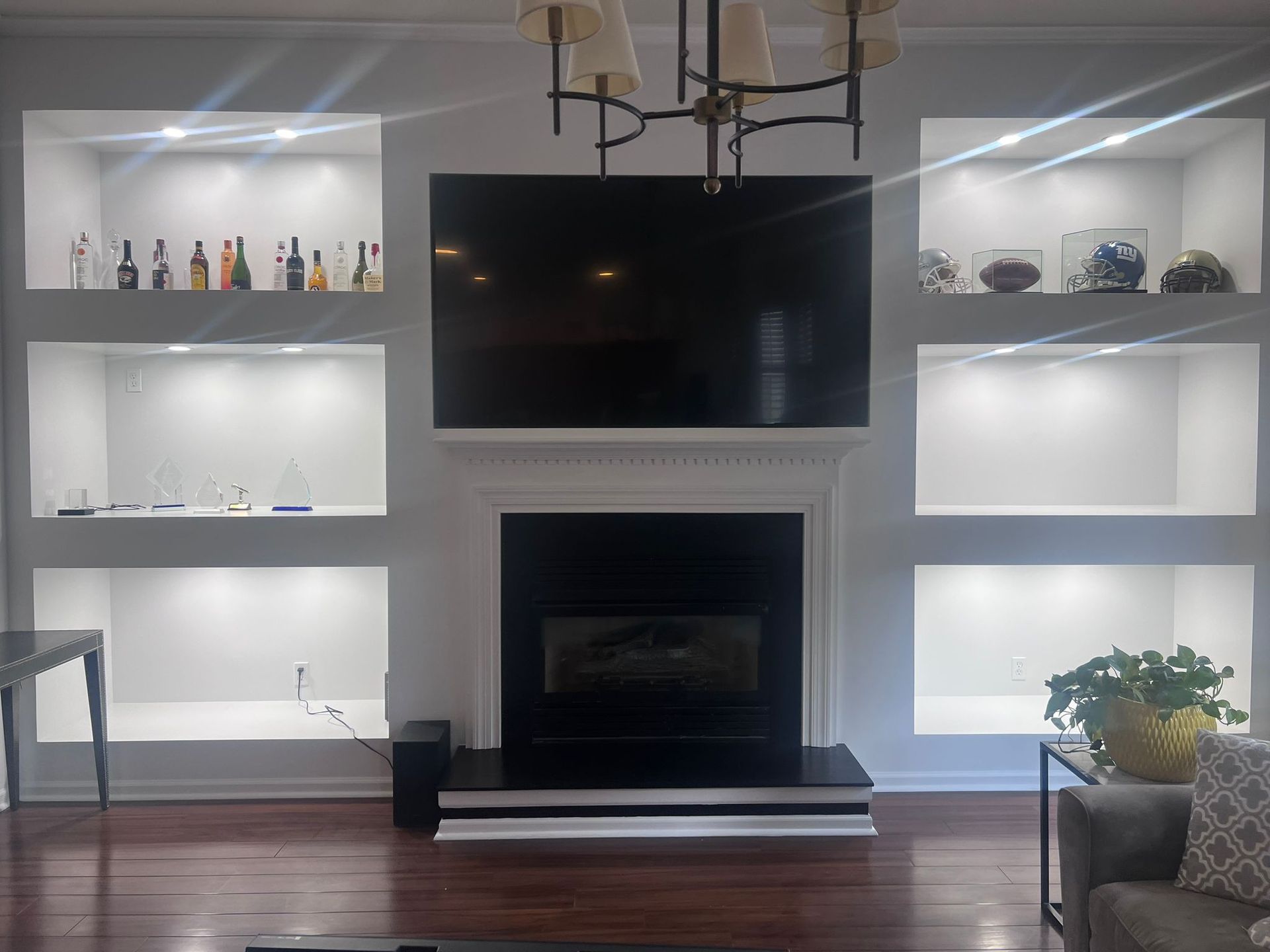Fireplace with built-in illuminated shelves on either side, holding decor and liquor bottles, a TV above the fireplace.