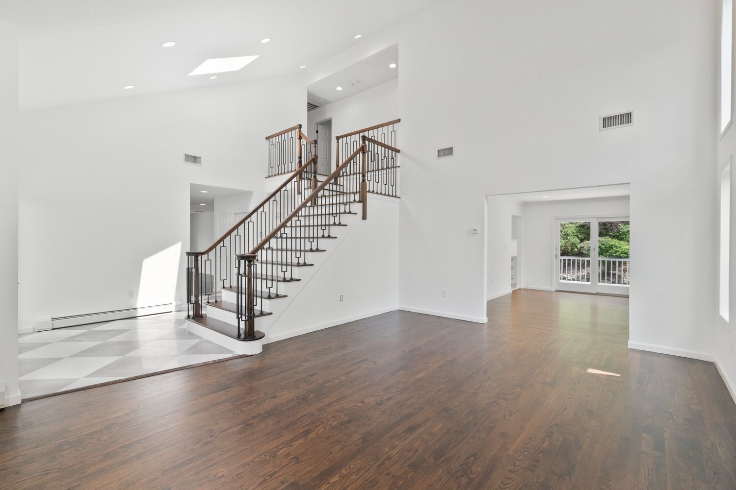 Spacious, bright interior with hardwood floors, a staircase, and access to an outdoor deck.