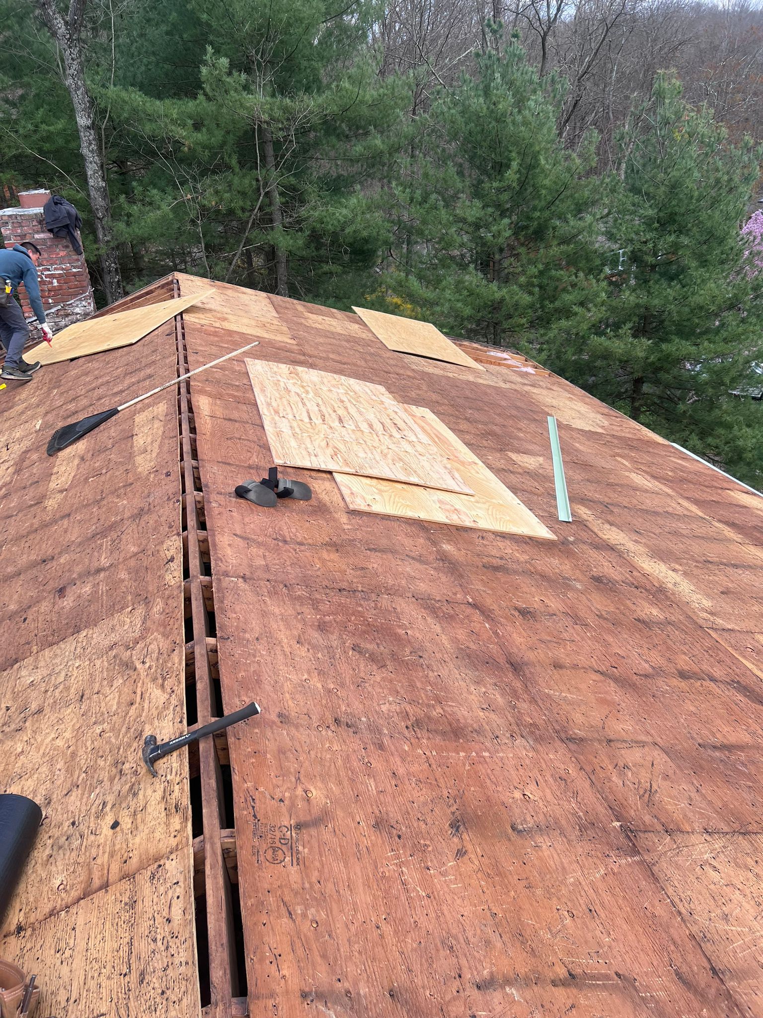 Roof with missing shingles, exposing wooden underlayment, and a worker by a chimney.
