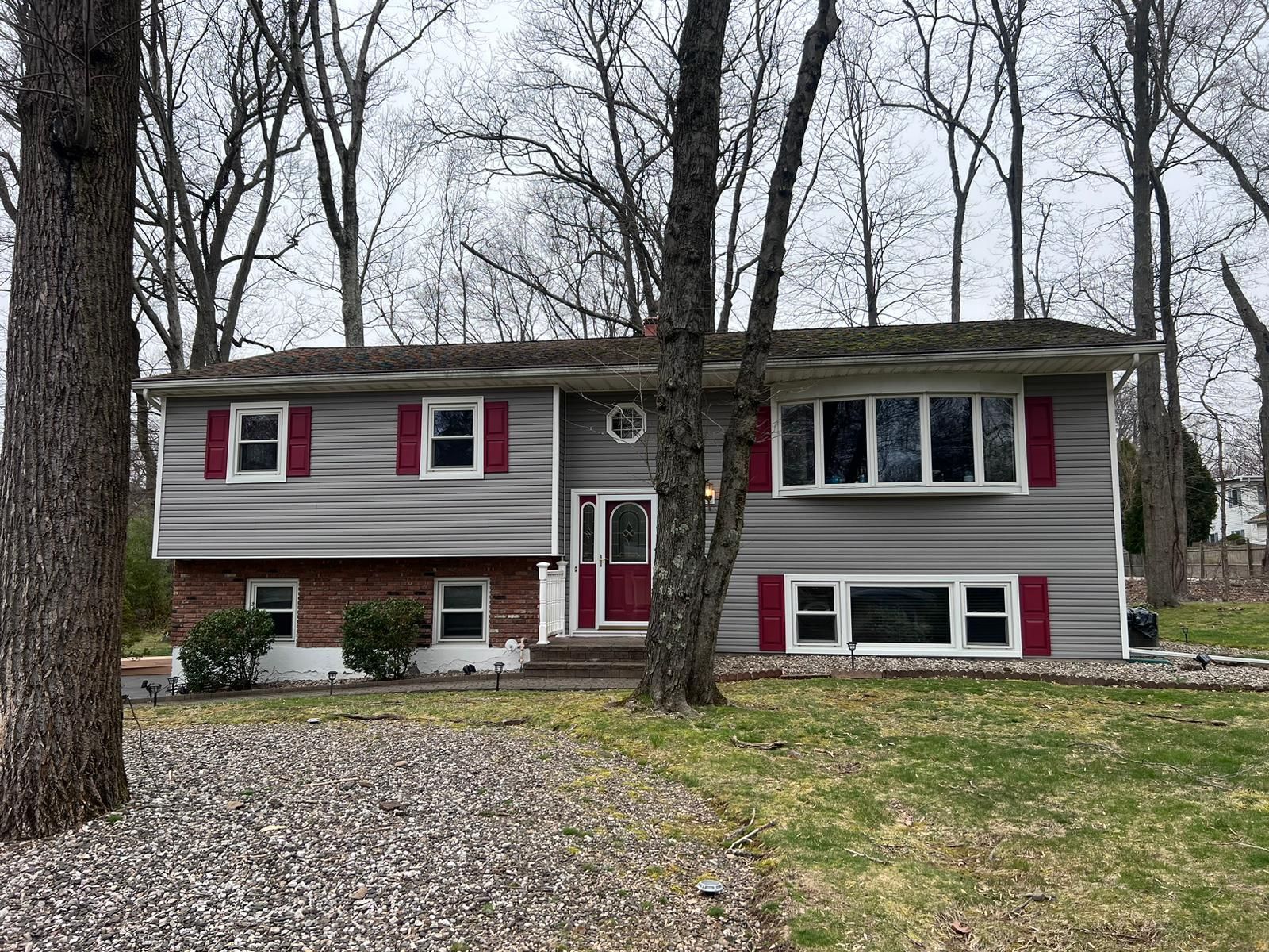 Gray and red house with trees in the yard on a cloudy day.