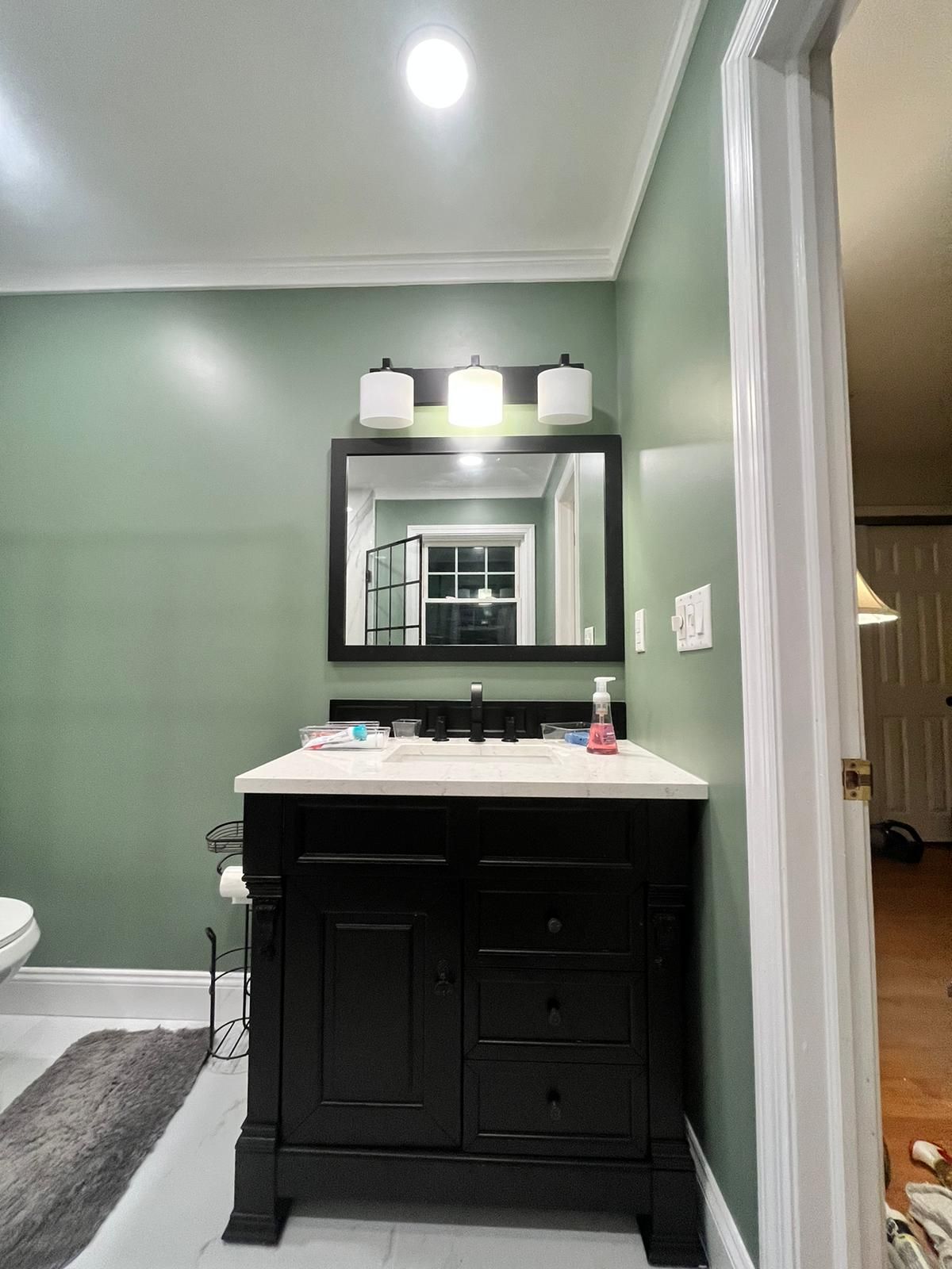 Black bathroom vanity with mirror and light fixture against green wall.