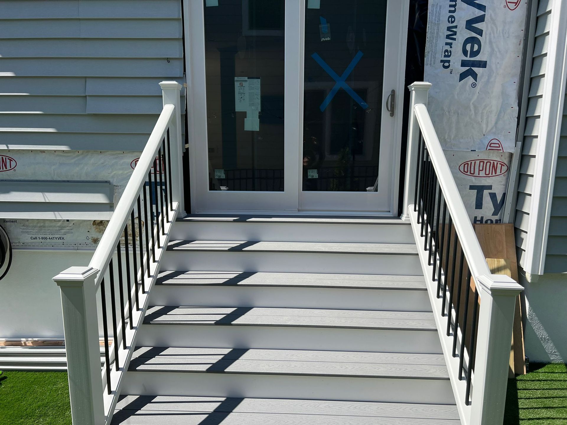Gray outdoor staircase leading to a white double door. Black railing.  House siding visible.